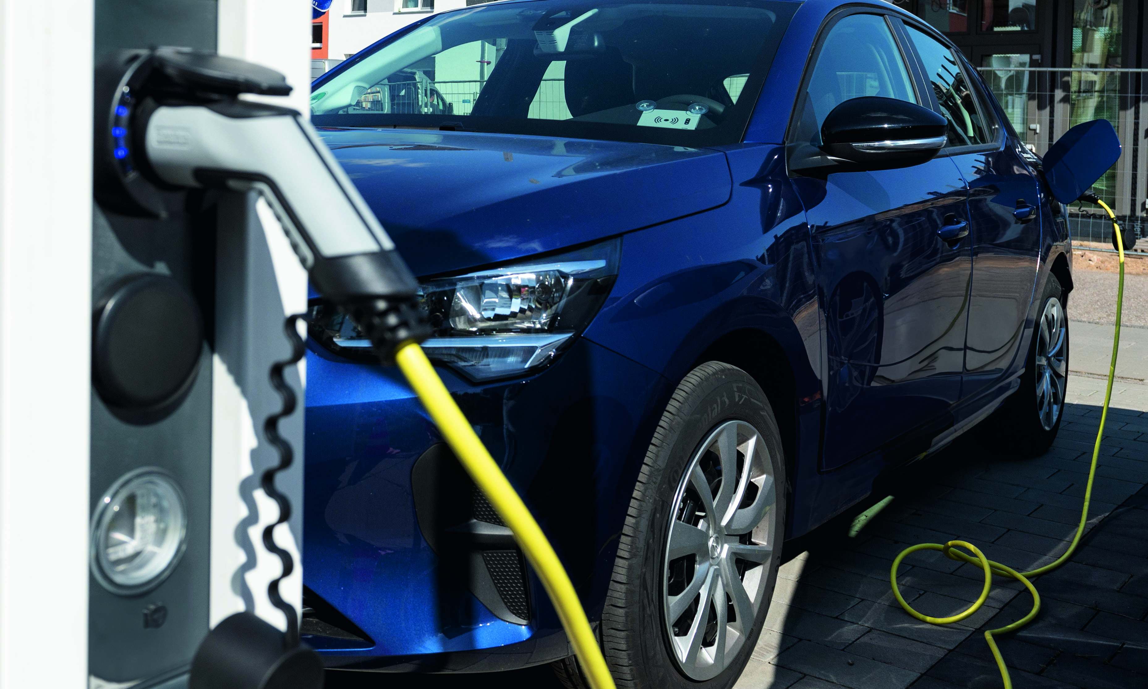 Blaues E-Auto mit E-Ladesäule im Vordergrund