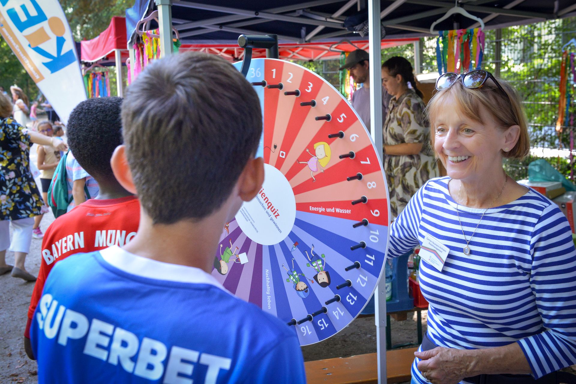 Eine Frau steht mit zwei Kindern an einem Glücksrad.