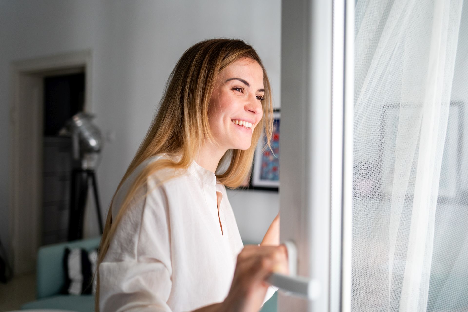 Frau öffnet das Fenster und schaut lächelnd nach draussen.