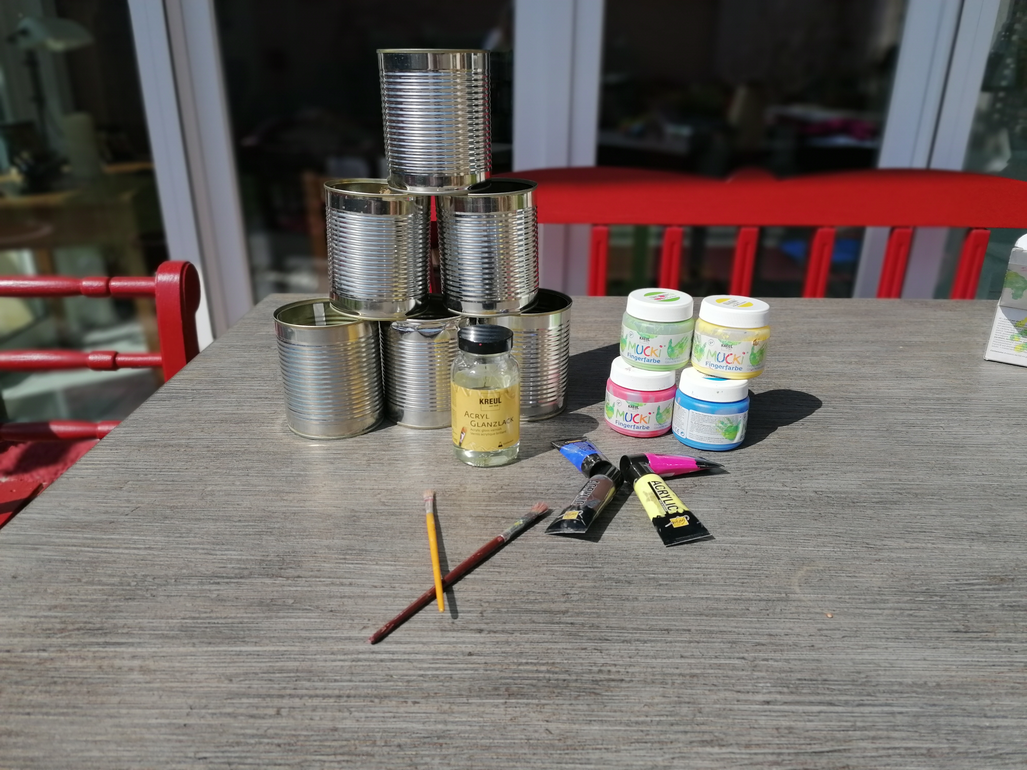 Dosen, Pinsel, Kleber und Farbe stehen und liegen auf dem Tisch.