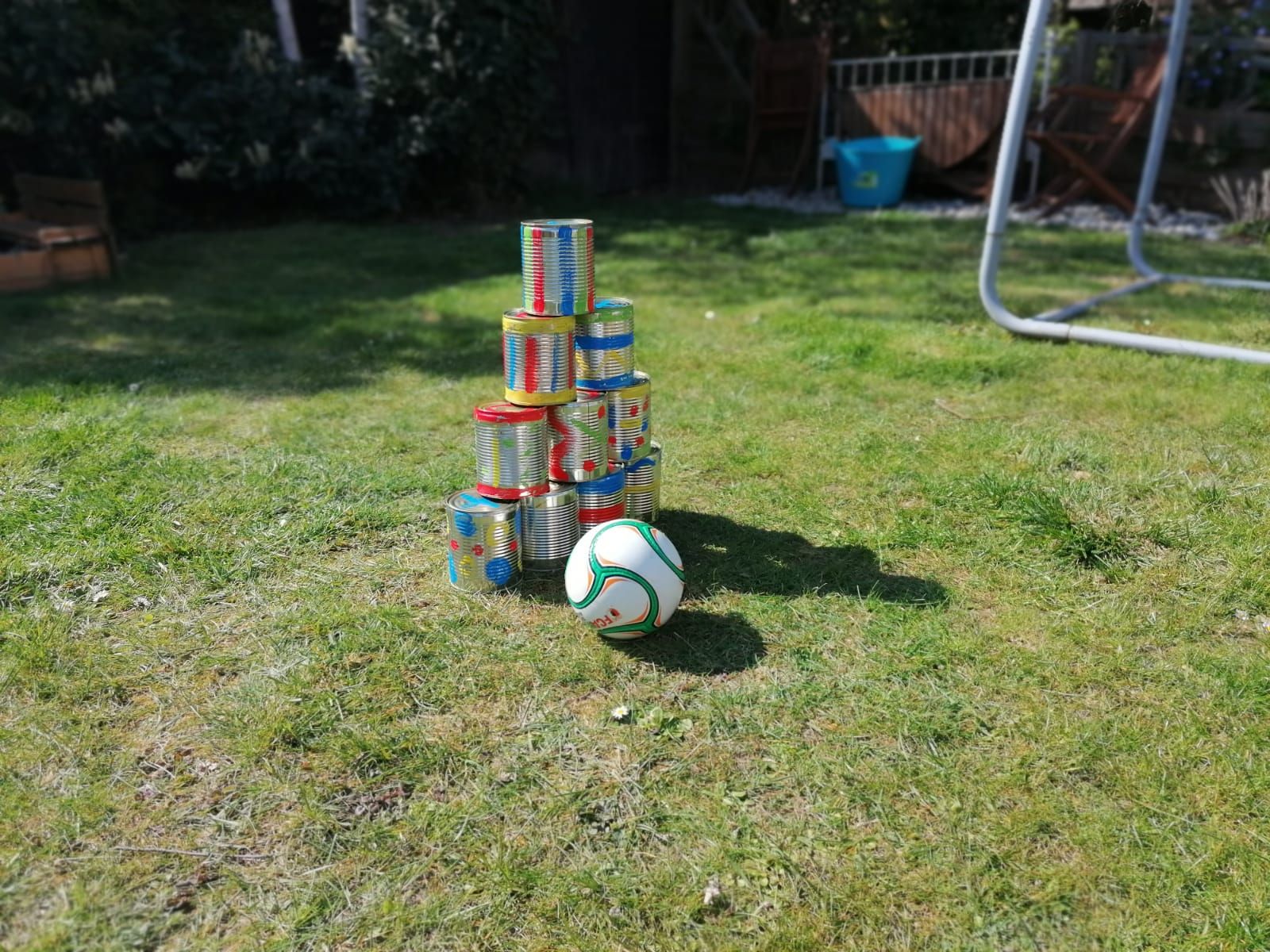 Auf einer Wiese sind bunte Dosen zu einer Pyramide aufgebaut. Davor liegt ein Ball.