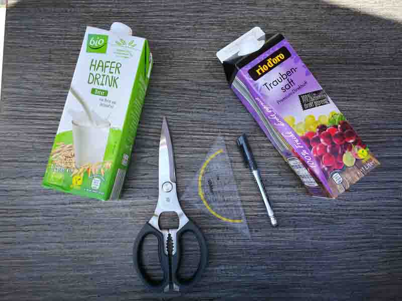 Milch- und Saft-Verpackung, Schere, Geo-Dreieck und Stift liegen auf einem Tisch.