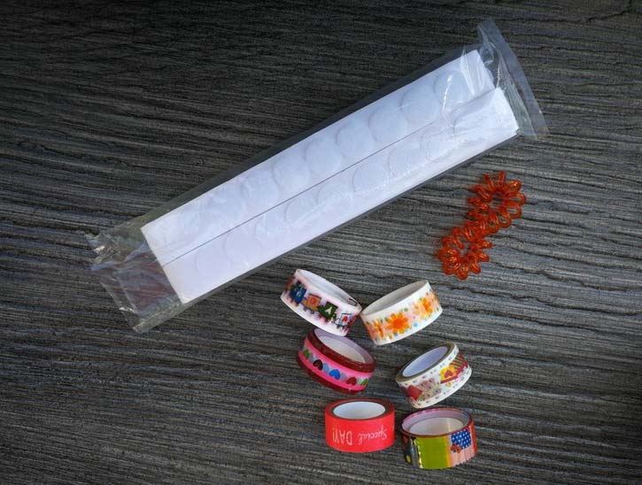 Klebepunkte, Washi-Tape und Haargummi liegen auf einem Tisch.