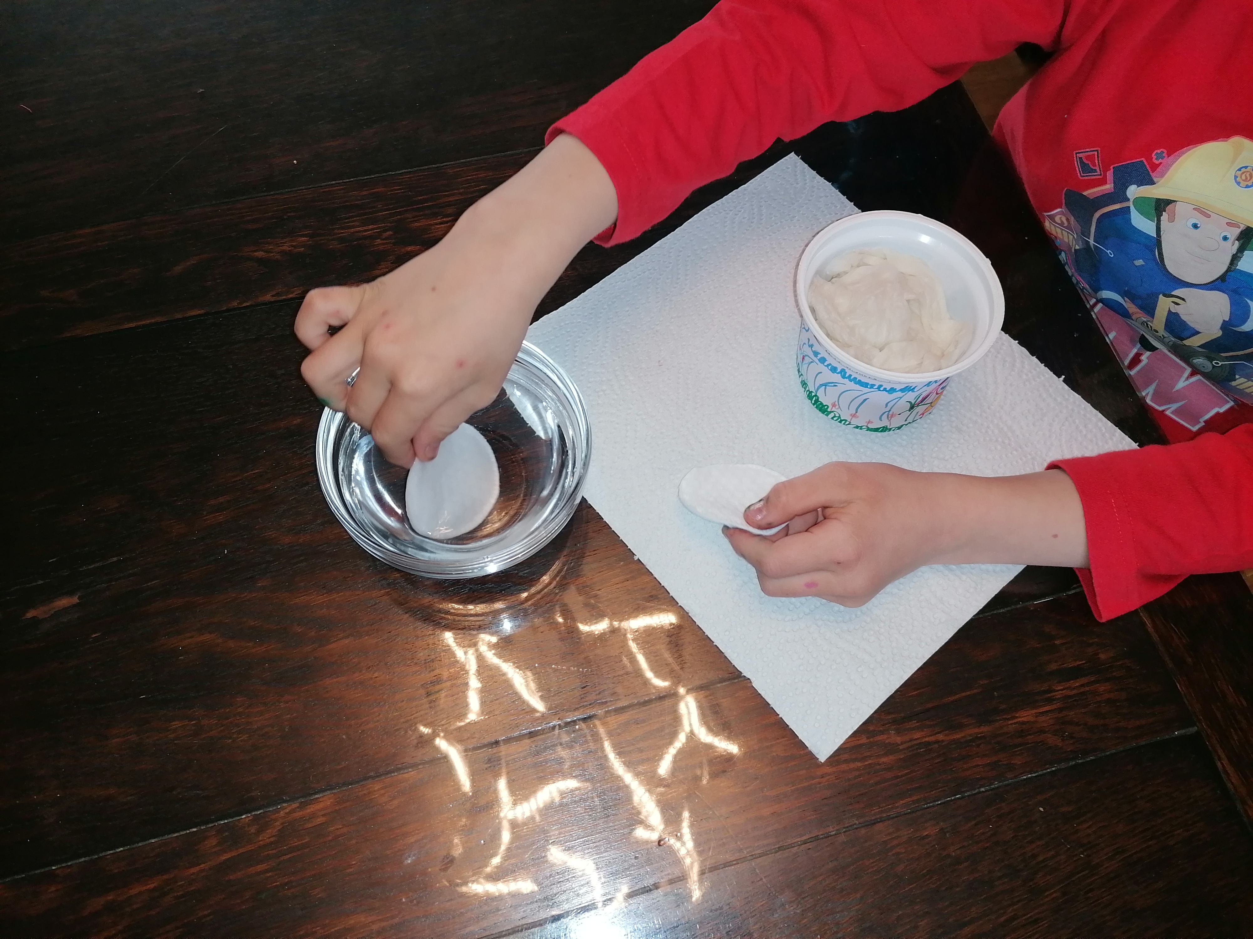 Ein Kind feuchtet Watte mit Wasser an und legt diese in einen leeren Joghurtbecher.