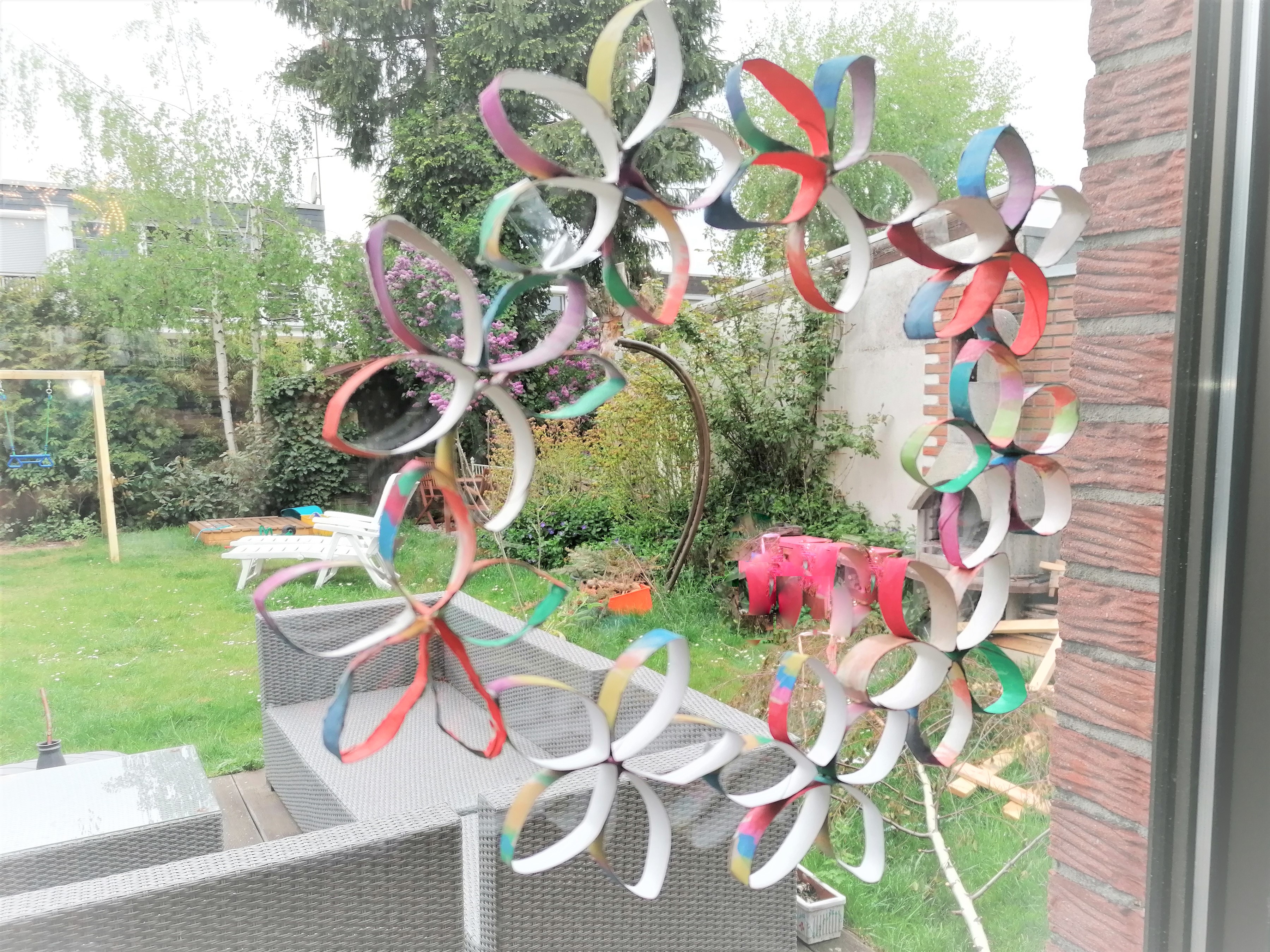 Papierblumen kleben als Kranz an einem Fenster.