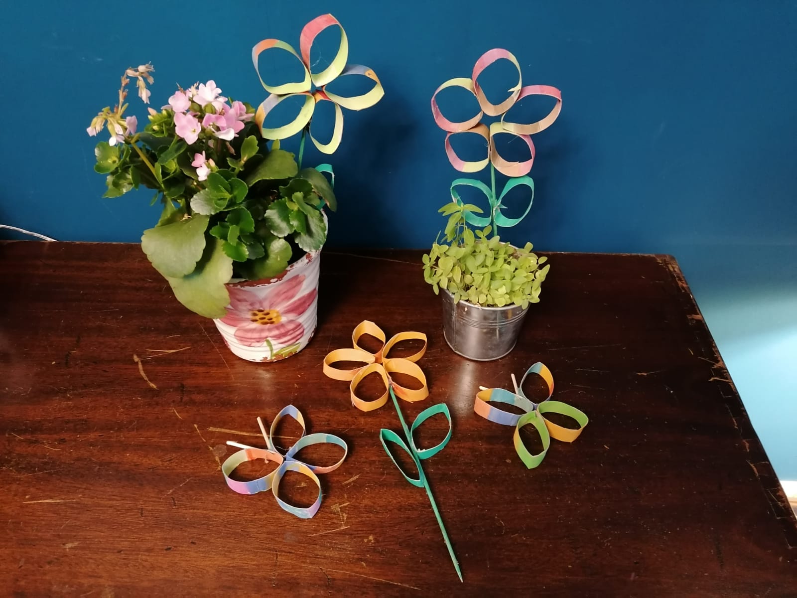 Blumentöpfe mit selbstgebastelten Blumensteckern aus Papier stehen auf einem Tisch.