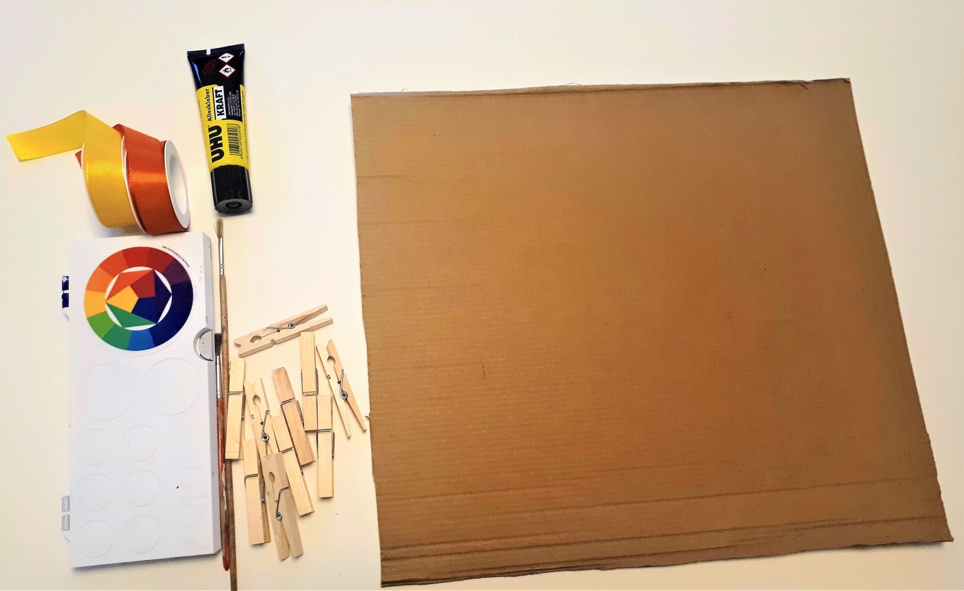 Wäscheklammern, Pappe, Kleber, Farbe und Bänder liegen auf einem Tisch.