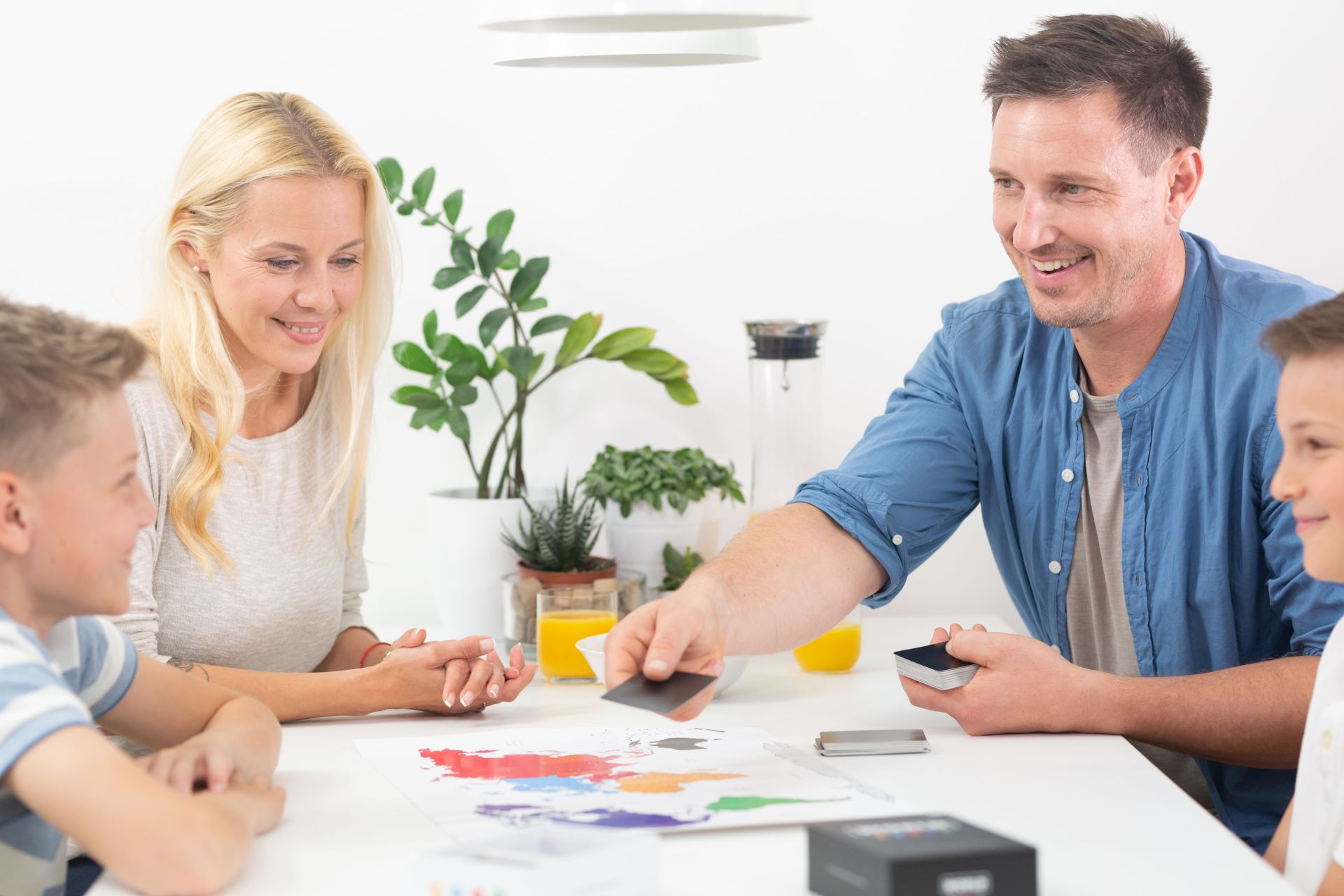 Vater, Mutter und zwei Kinder sitzen am Tisch und spielen ein Spiel.