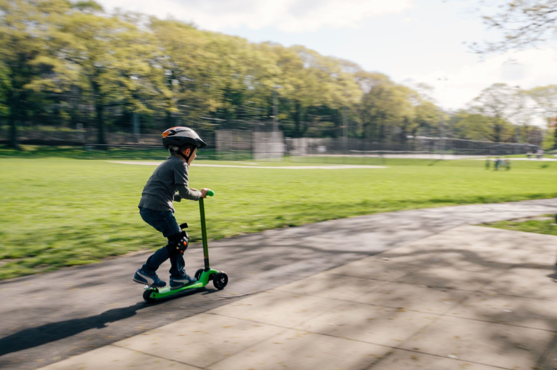 Ein Kind mit Helm fährt Tretroller im einem Park.