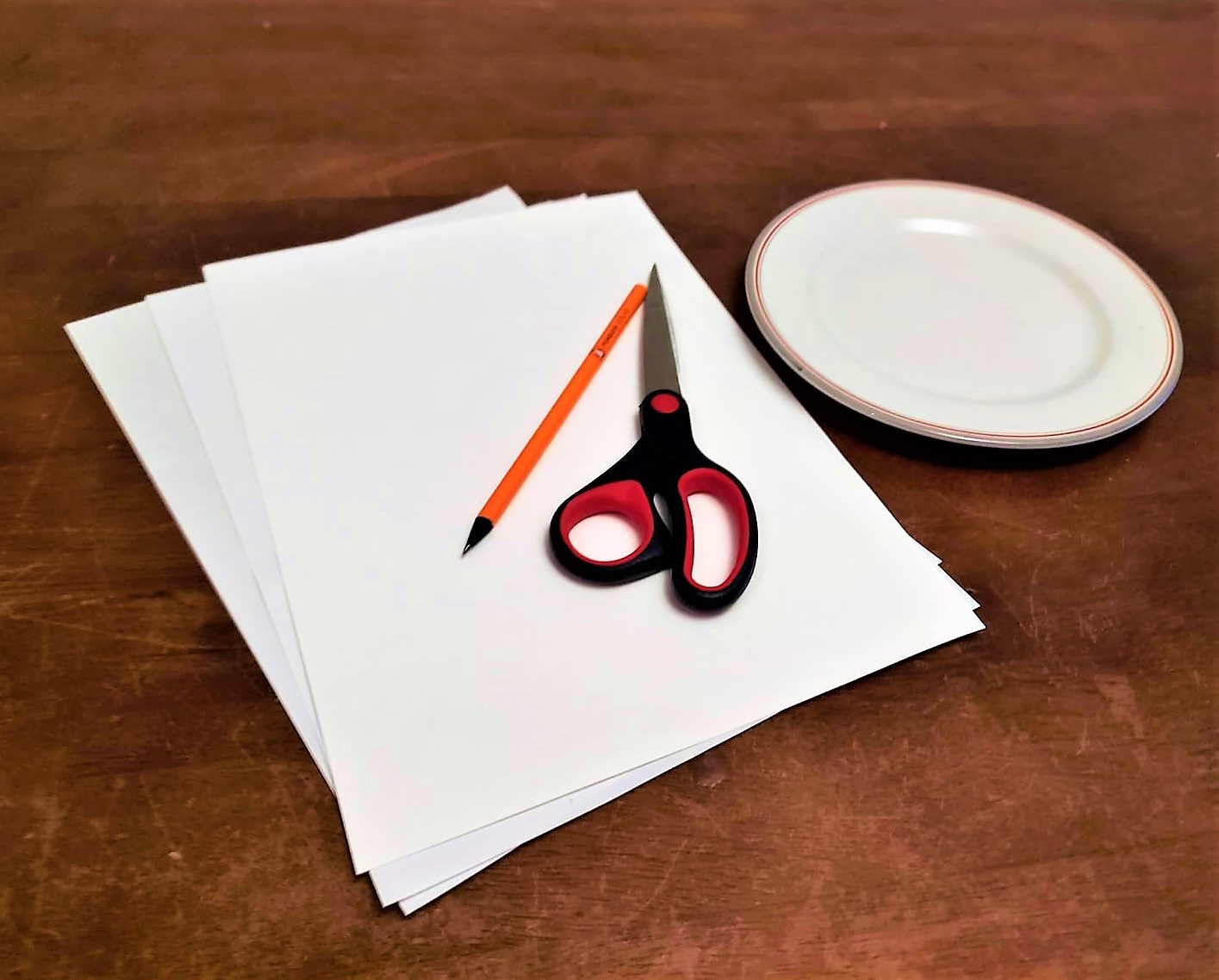 Papier, Stift, Schere und Teller liegen auf einem Tisch.