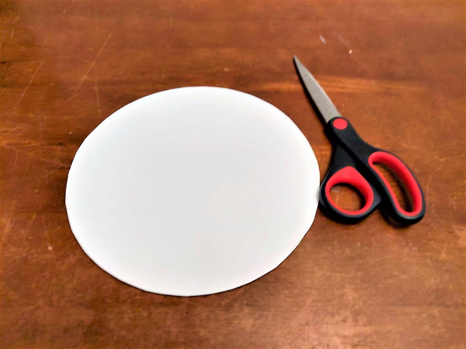 Ein Papierkreis und eine Schere liegen auf einem Tisch.