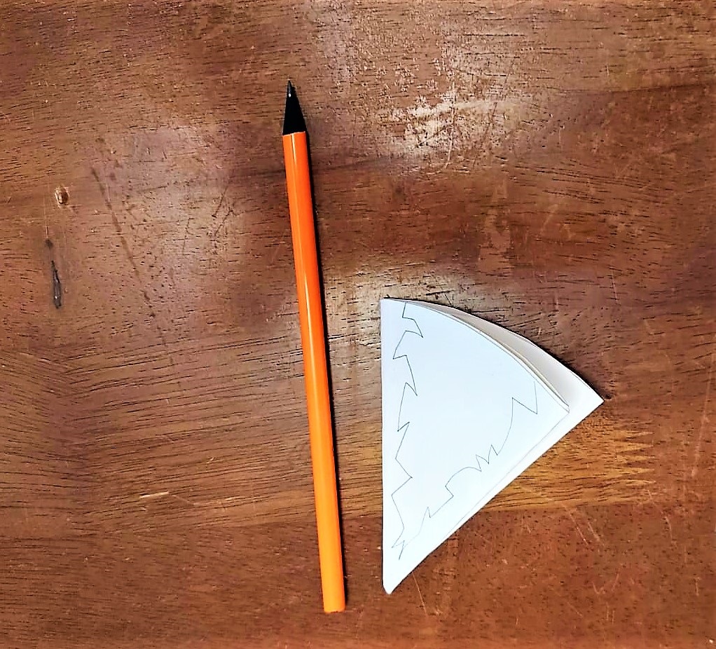 Ein Stift und ein gefaltetes Stück Papier liegen auf dem Tisch. Auf dem Papier ist ein Umriss aufgezeichnet.