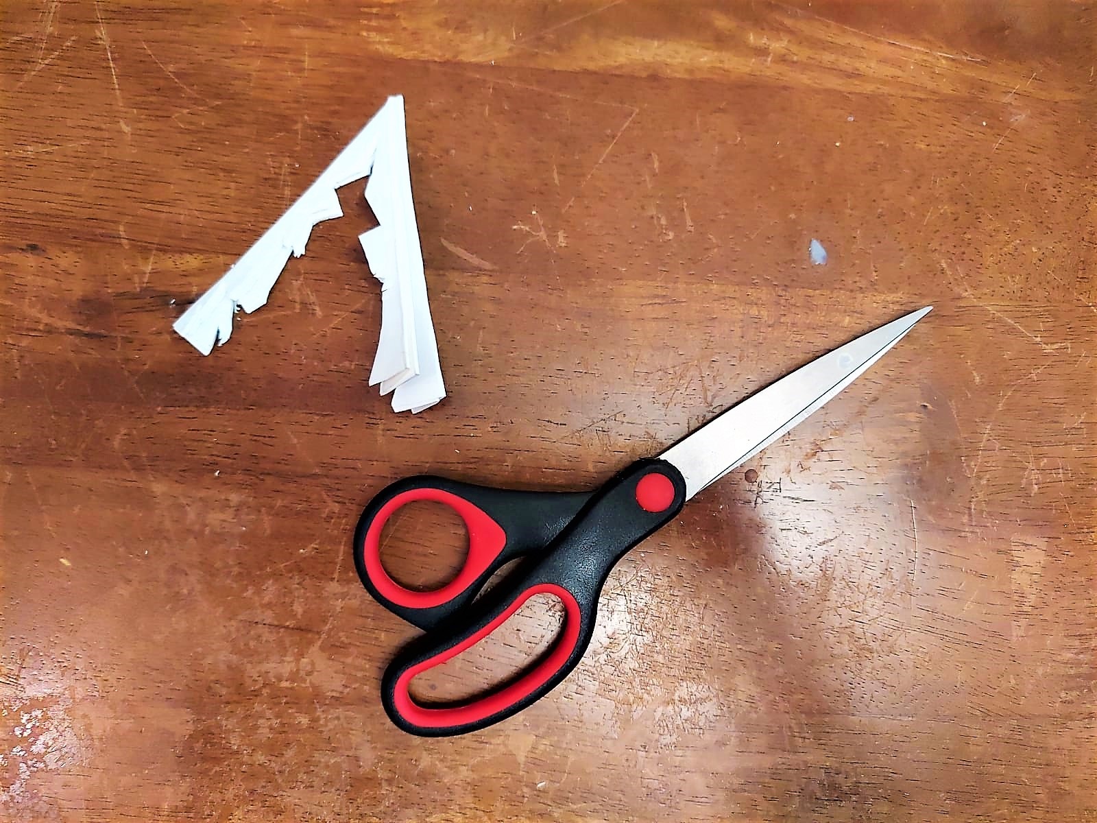 Eine Schere und ein geschnittenes Stück Papier liegen auf dem Tisch.