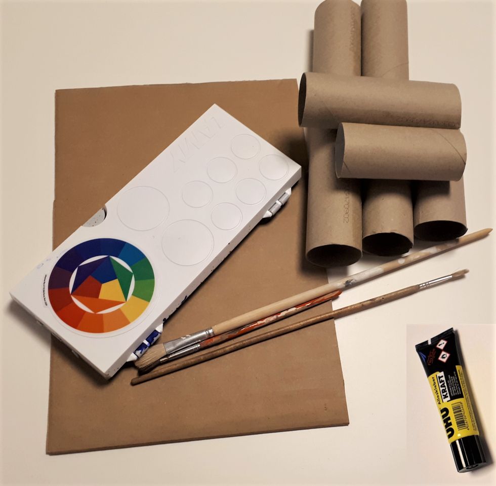 Papprollen, Pappe, Klebstoff, Farbe und Pinsel liegen auf einem Tisch.