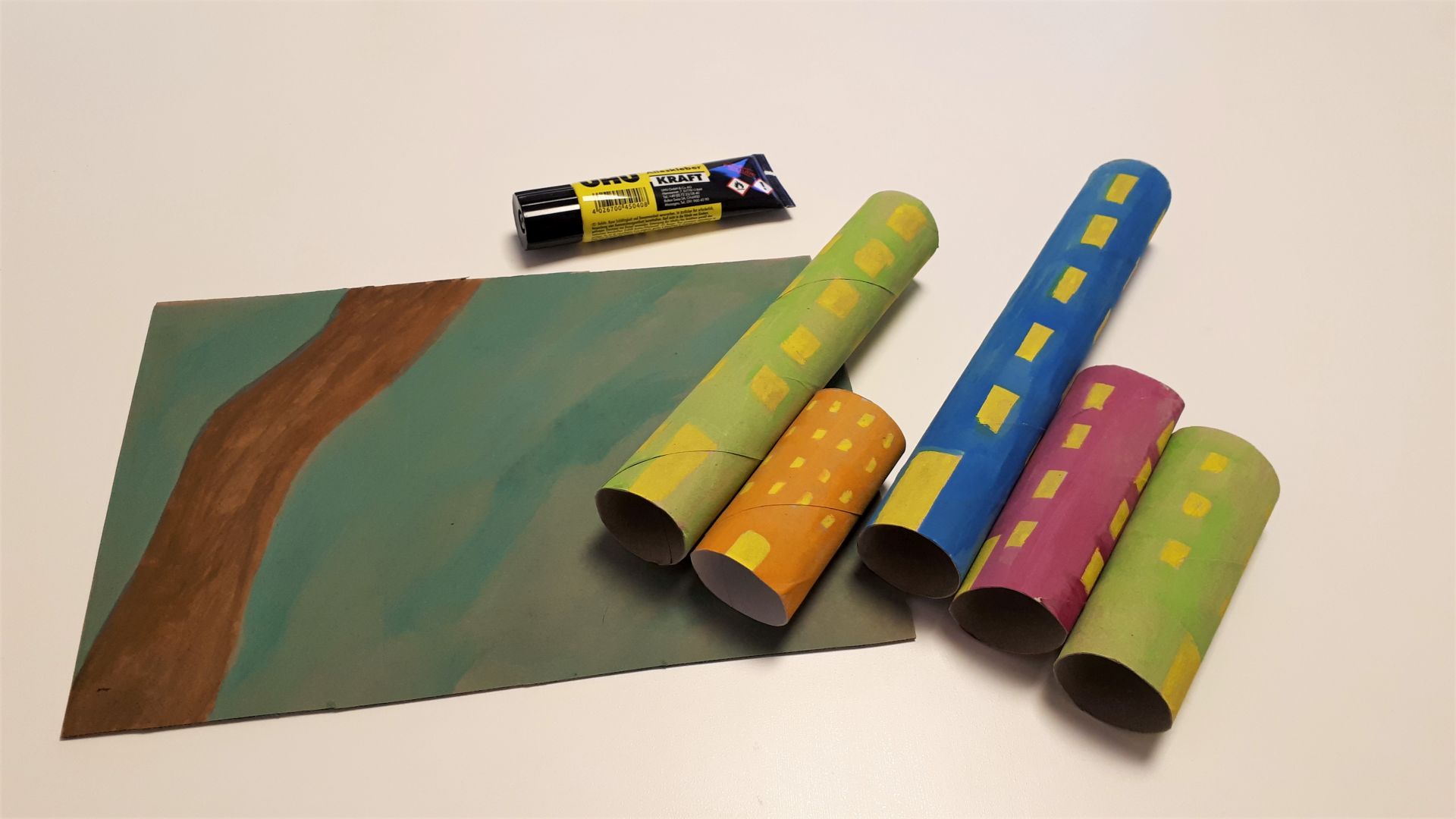 Bemalte Pappe, bemalte Papprollen und Kleber liegen auf einem Tisch.