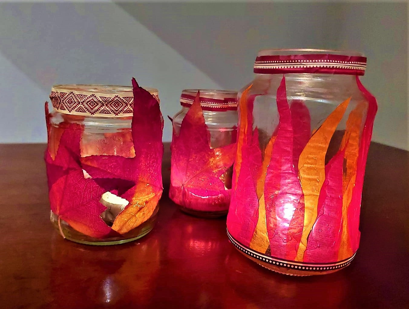 Mit Transparentpapier beklebte Einweggläser stehen auf dem Tisch. In den Gläsern brennt ein Teelicht.