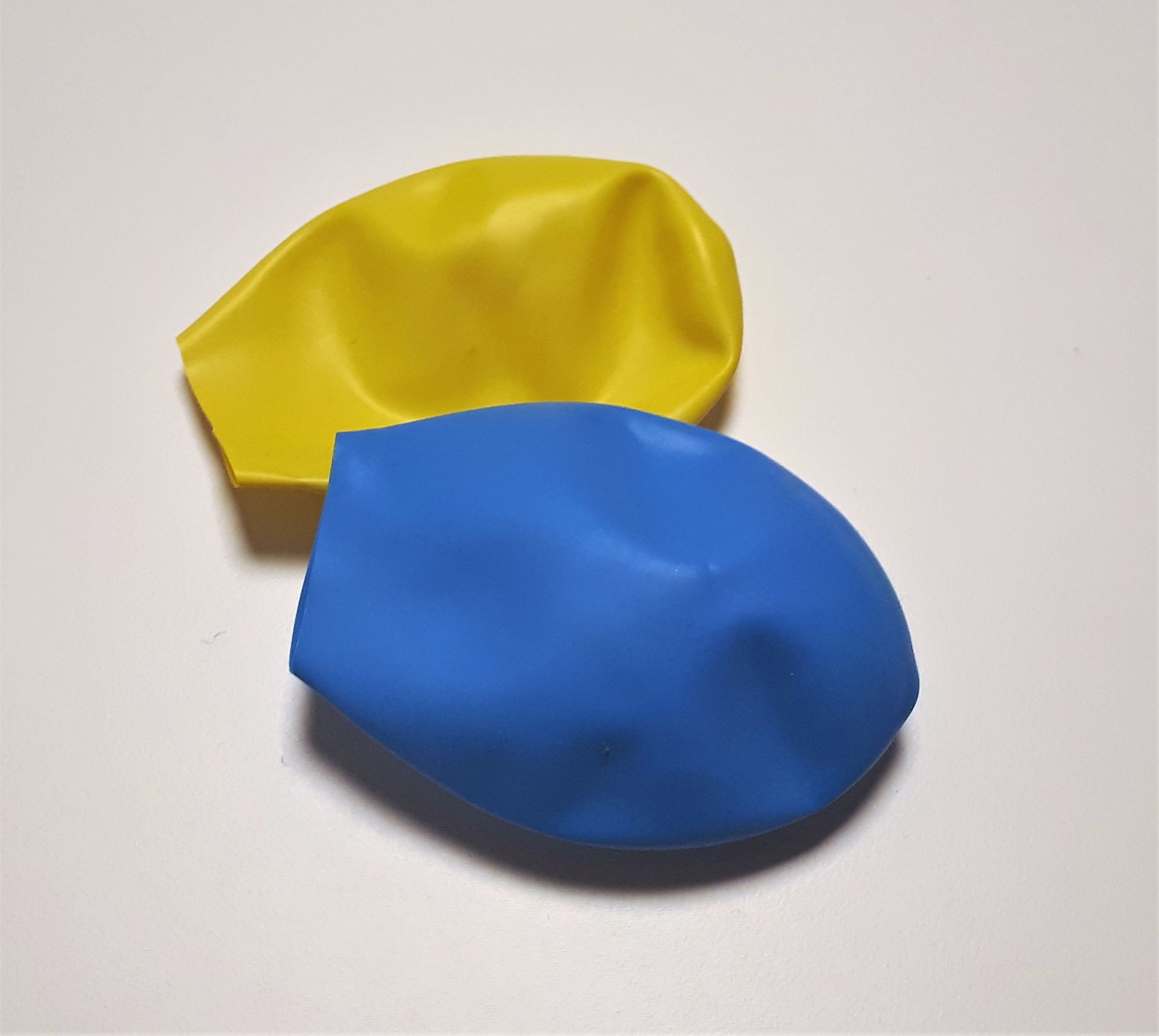 Ein gelber und ein blauer Luftballon liegen aufgeschnitten auf einem Tisch.