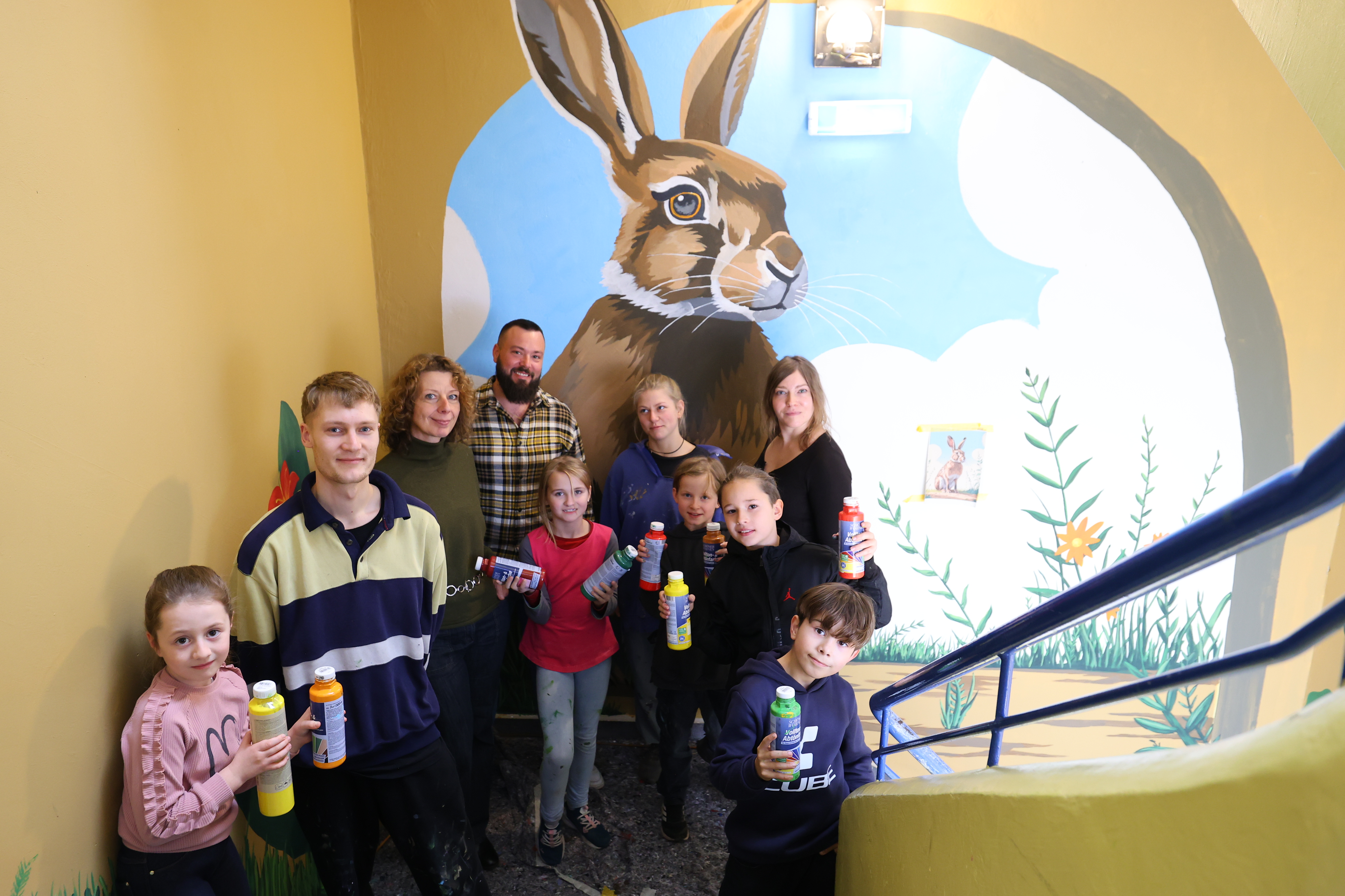 Gruppe von Kindern und Jugendlichen steht in einem Treppenhaus mit Farbflaschen in der Hand. Im Hintergrund ist gemaltes Wandbild mit einem Hasen.