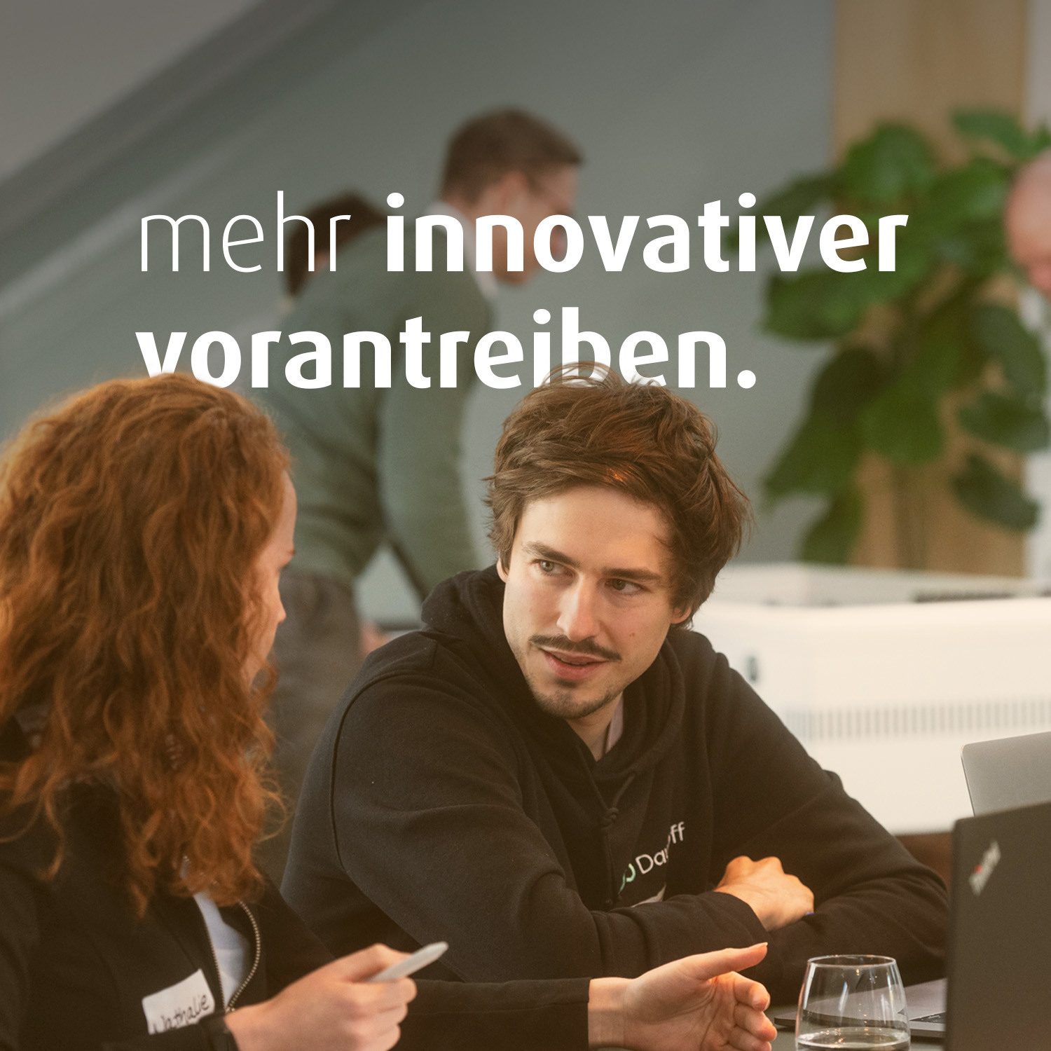 Eine Frau und ein Mann sitzen nebeneinander an einem Tisch. Vor ihnen stehen Laptops. Im Bild steht der Text "mehr innovativer vorantreiben".