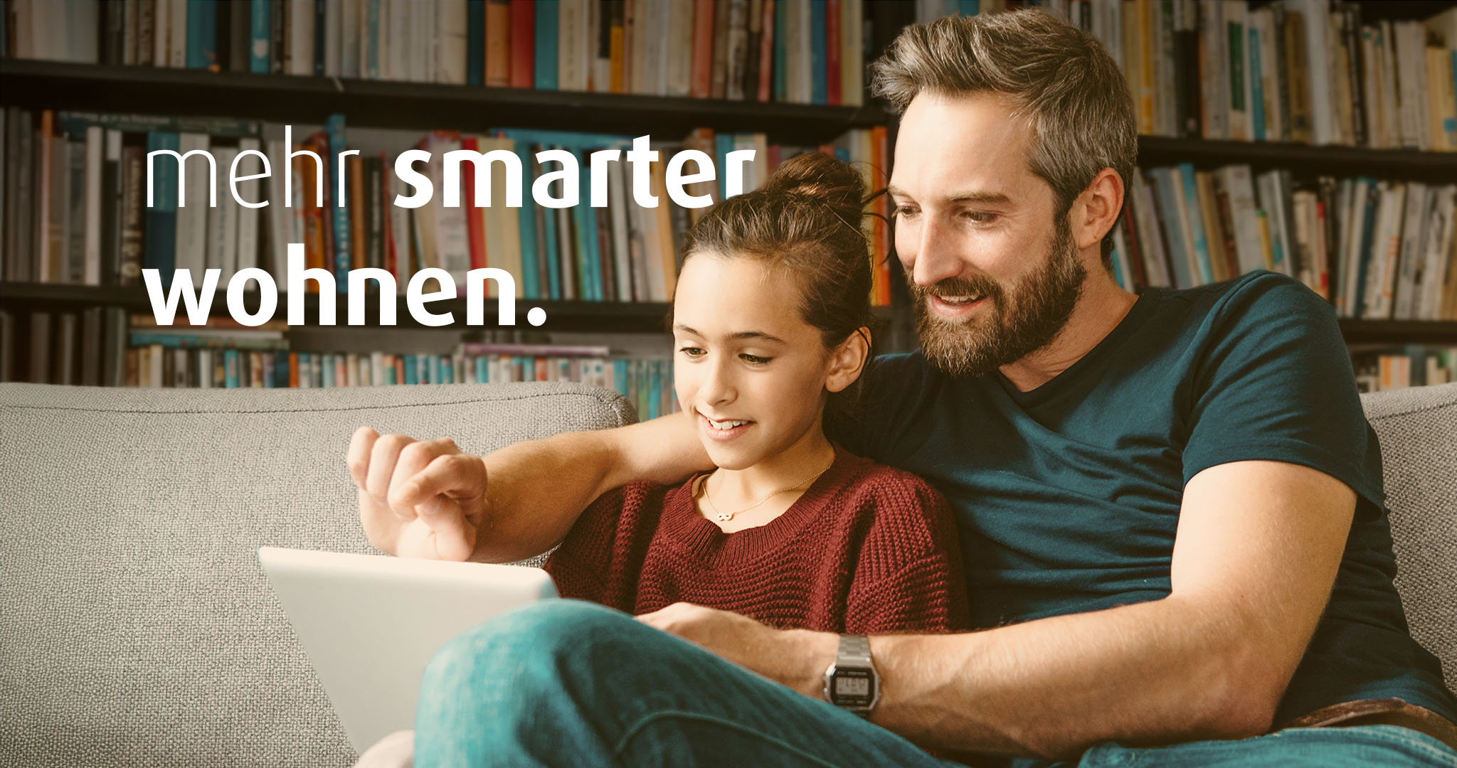 Ein Mann und ein Mädchen sitzen auf dem Sofa. Sie schauen zusammen auf ein Tablet. Auf dem Bild steht der Text "mehr smarter wohnen".