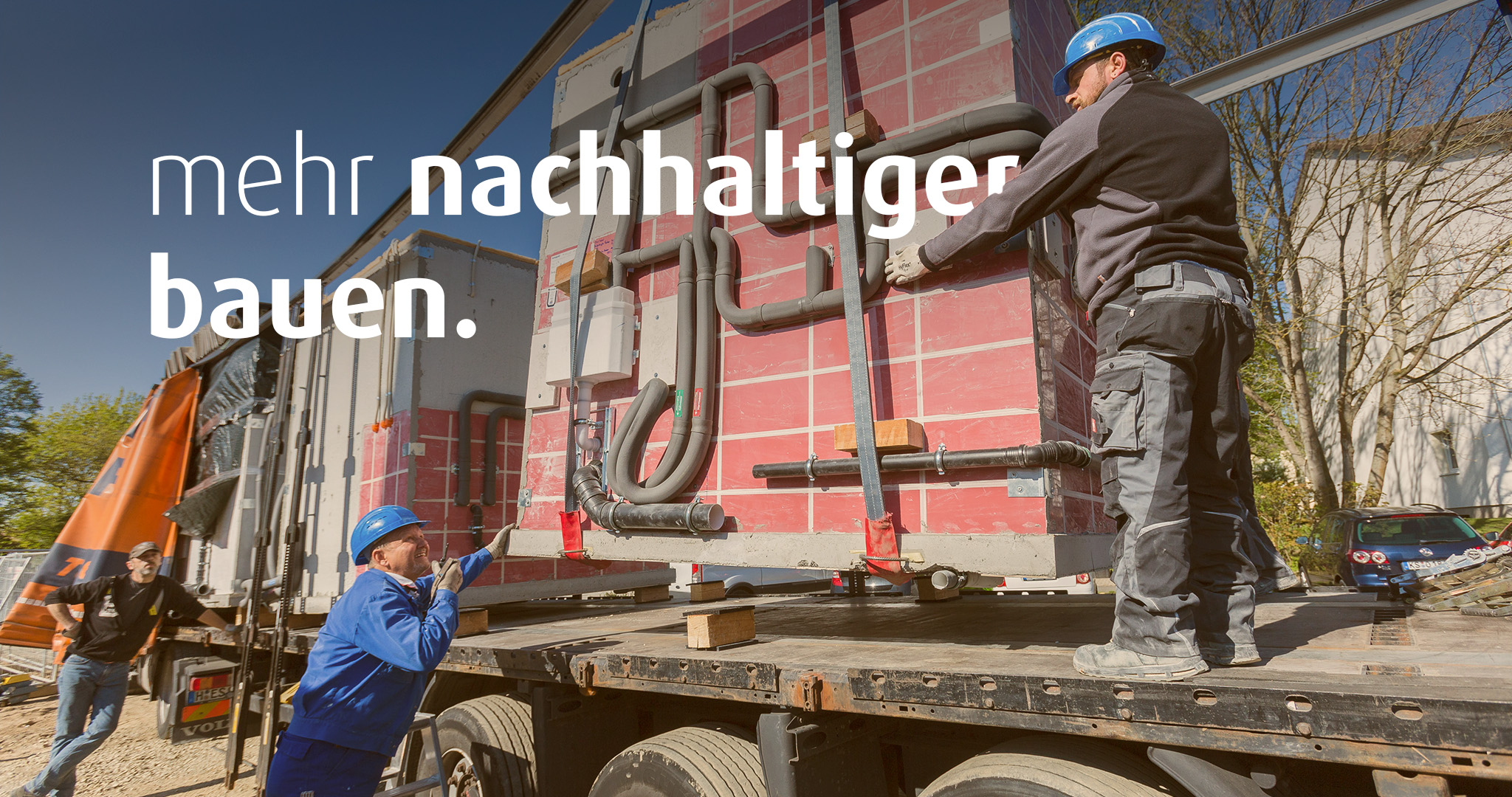 Zwei Männer in Baustellenkleidung entladen einen Lastwagen, der ein Modul für die Baustelle angeliefert hat. Auf dem Bild steht der Text "mehr nachhaltiger bauen".