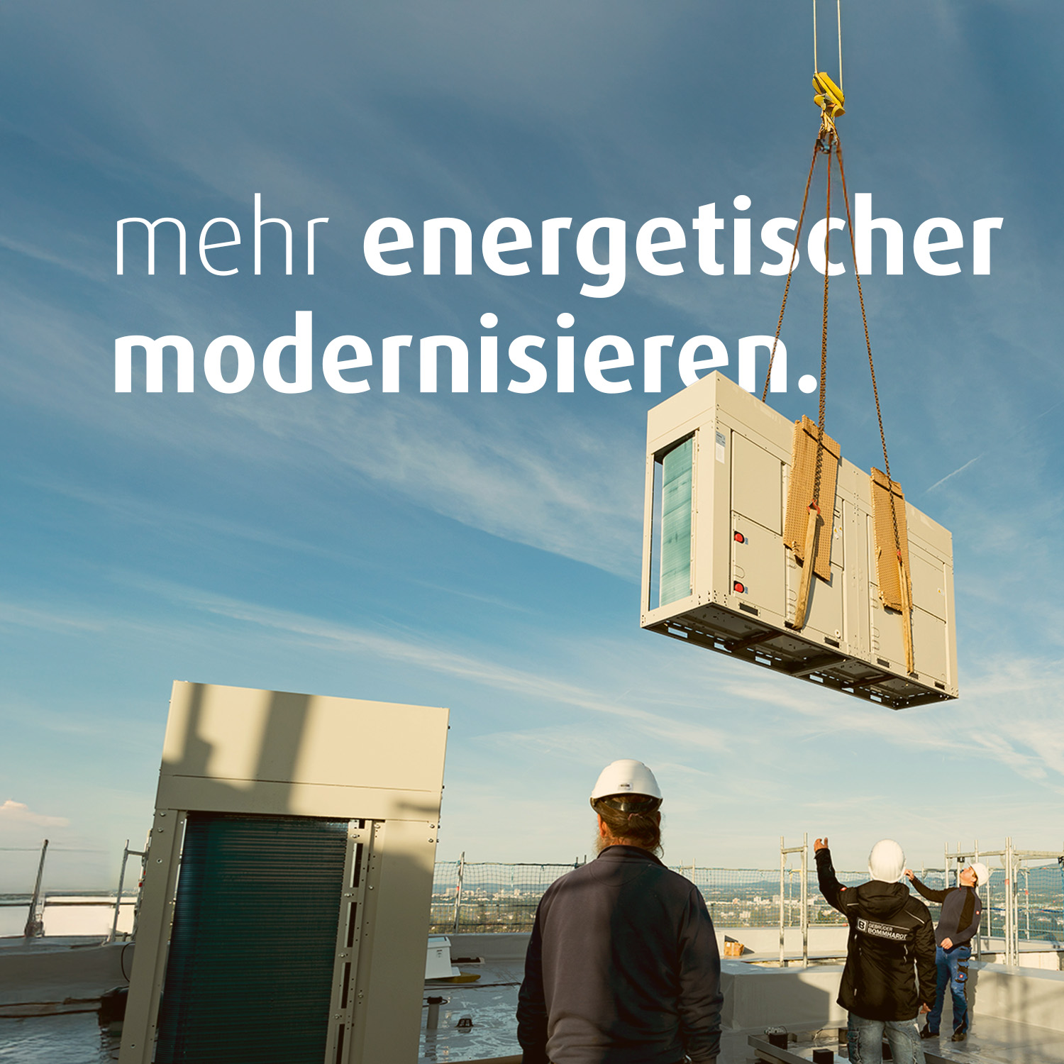 Mit einem Kran wird eine Wärmepumpe auf ein Hausdach gehoben. Vier Bauarbeiter stehen auf dem Dach. Auf dem Bild steht der Text "mehr energetischer modernisieren".