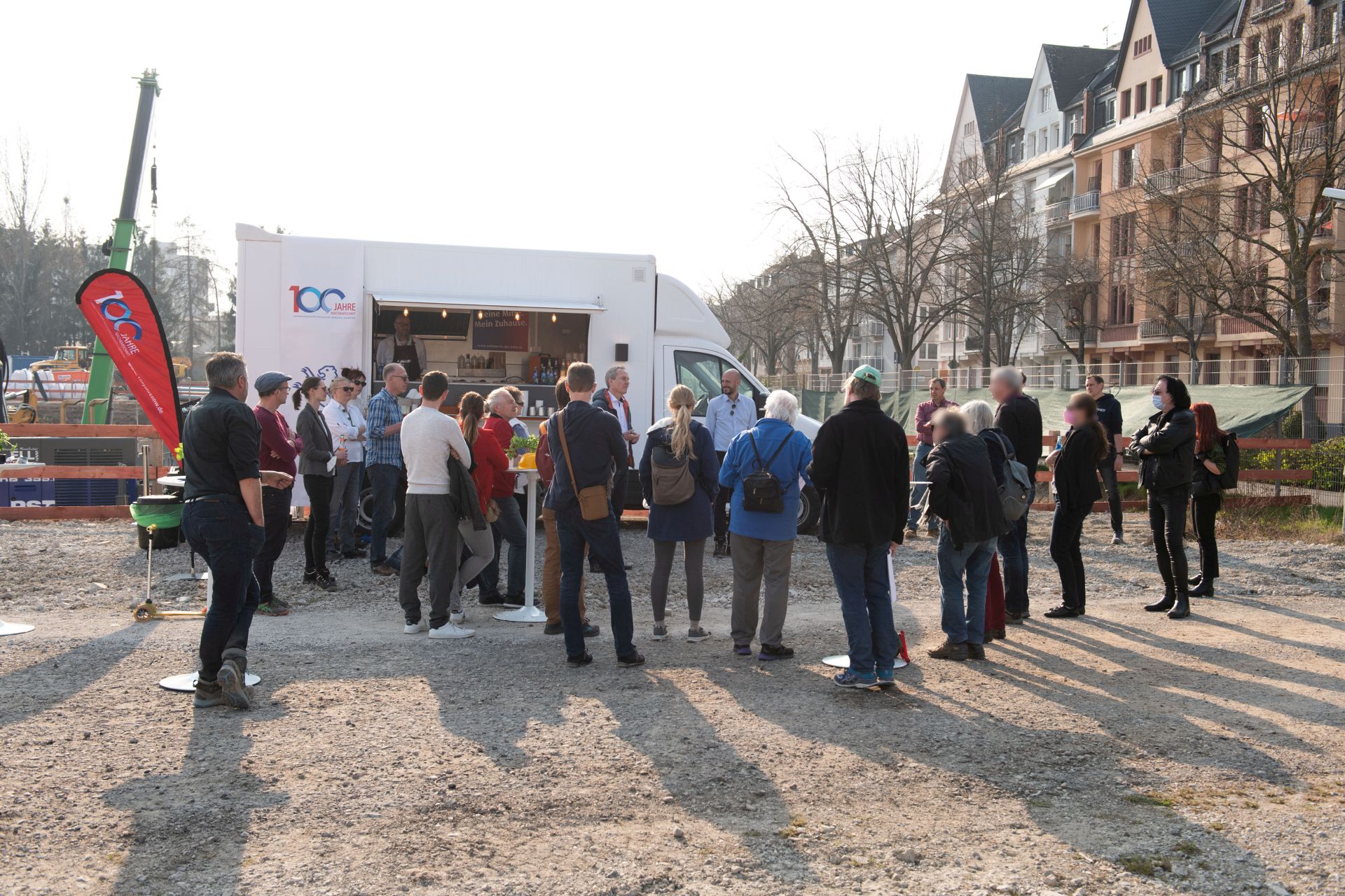 Gruppe von Menschen auf Brachfläche vor Häusern und Van