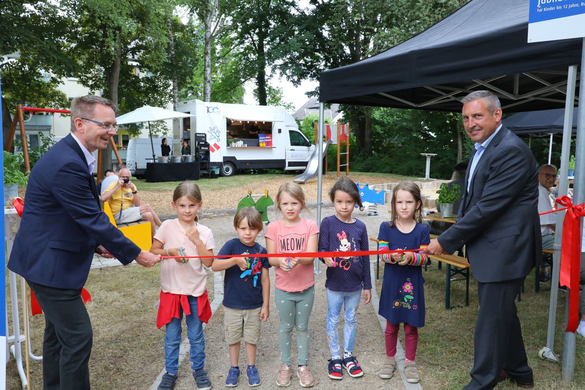 Zwei Männer und fünf Kinder schneiden ein Band durch