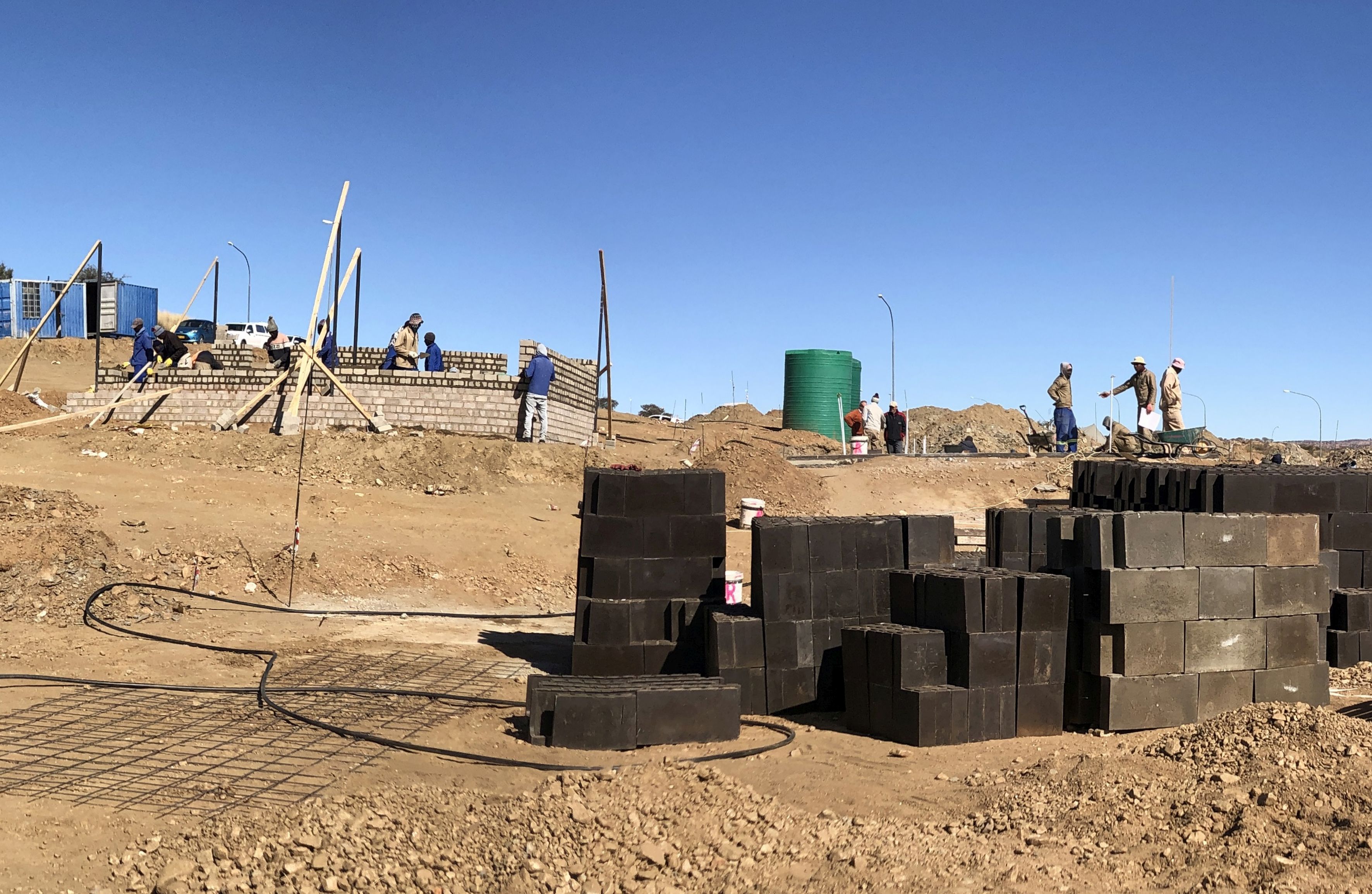 Bauarbeiter bauen zwei Häuser, im Vordergrund Mauersteine