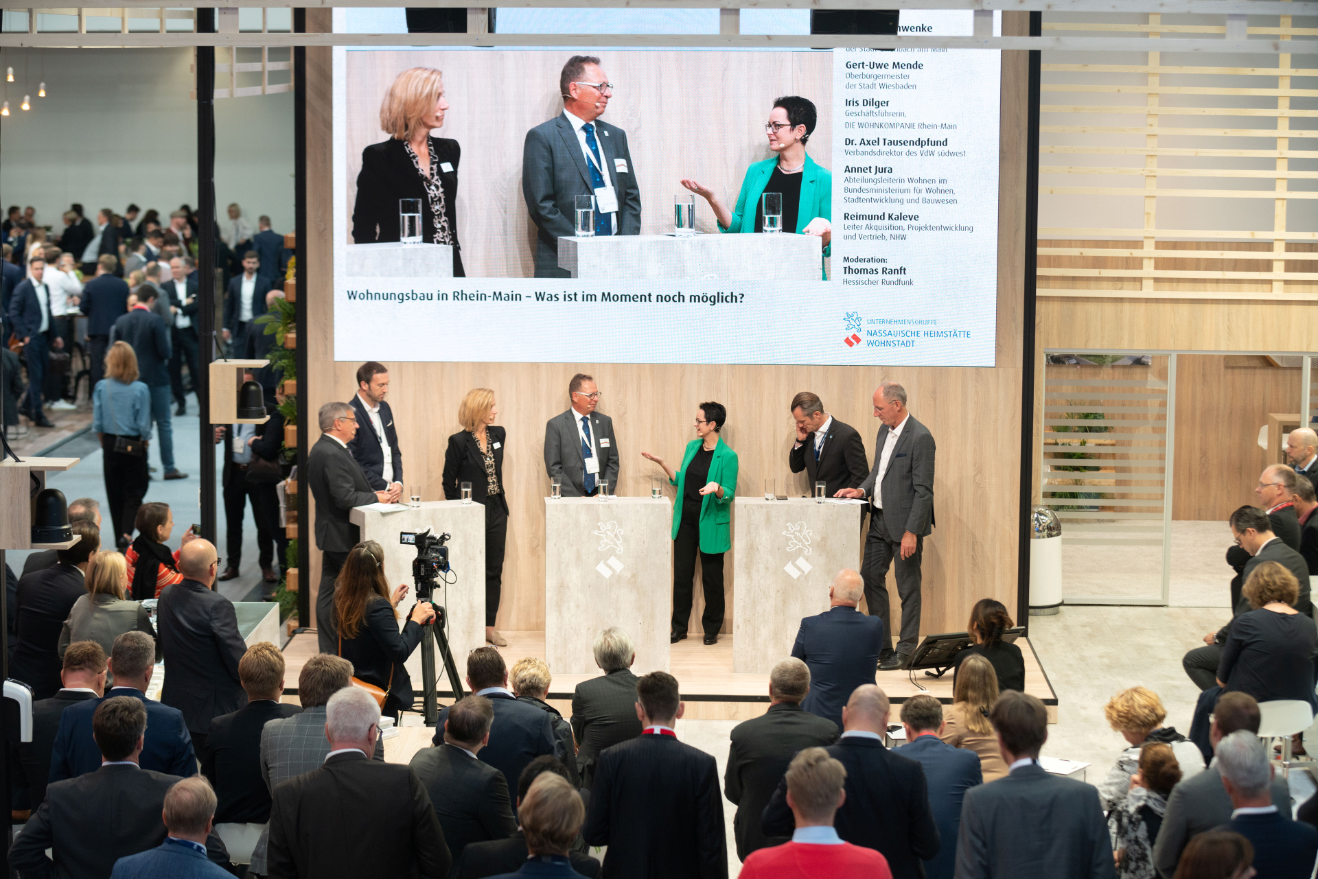 Menschen diskutieren miteinander, Zuschauer sehen zu, wird auf großen Screen übertragen