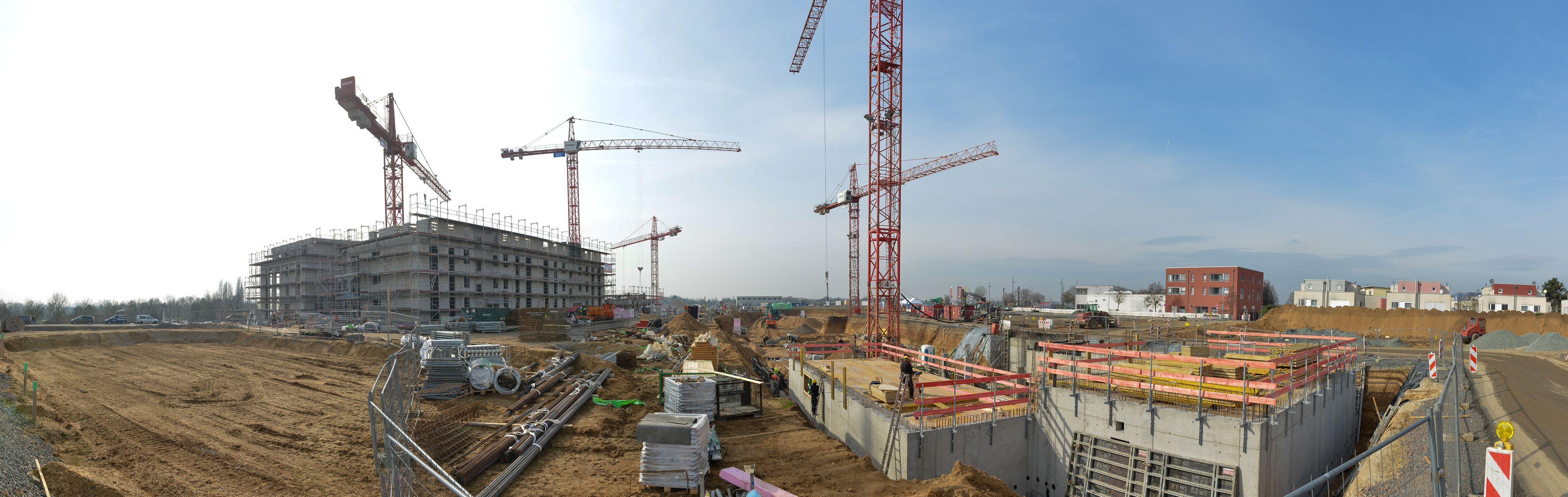 Überblicksfoto über die Baustelle mit Baugrube, Kränen sowie einem weiter fortgeschrittenen Rohbau