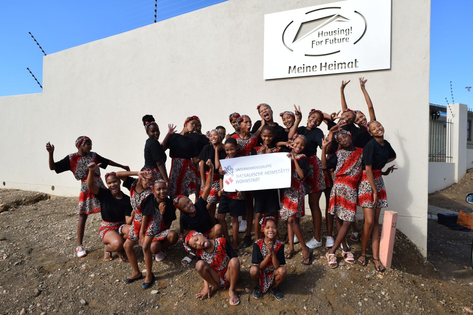 Eine Gruppe bunt gekleideter, jubelnder Mädchen hält das NHW-Logo in die Kamera