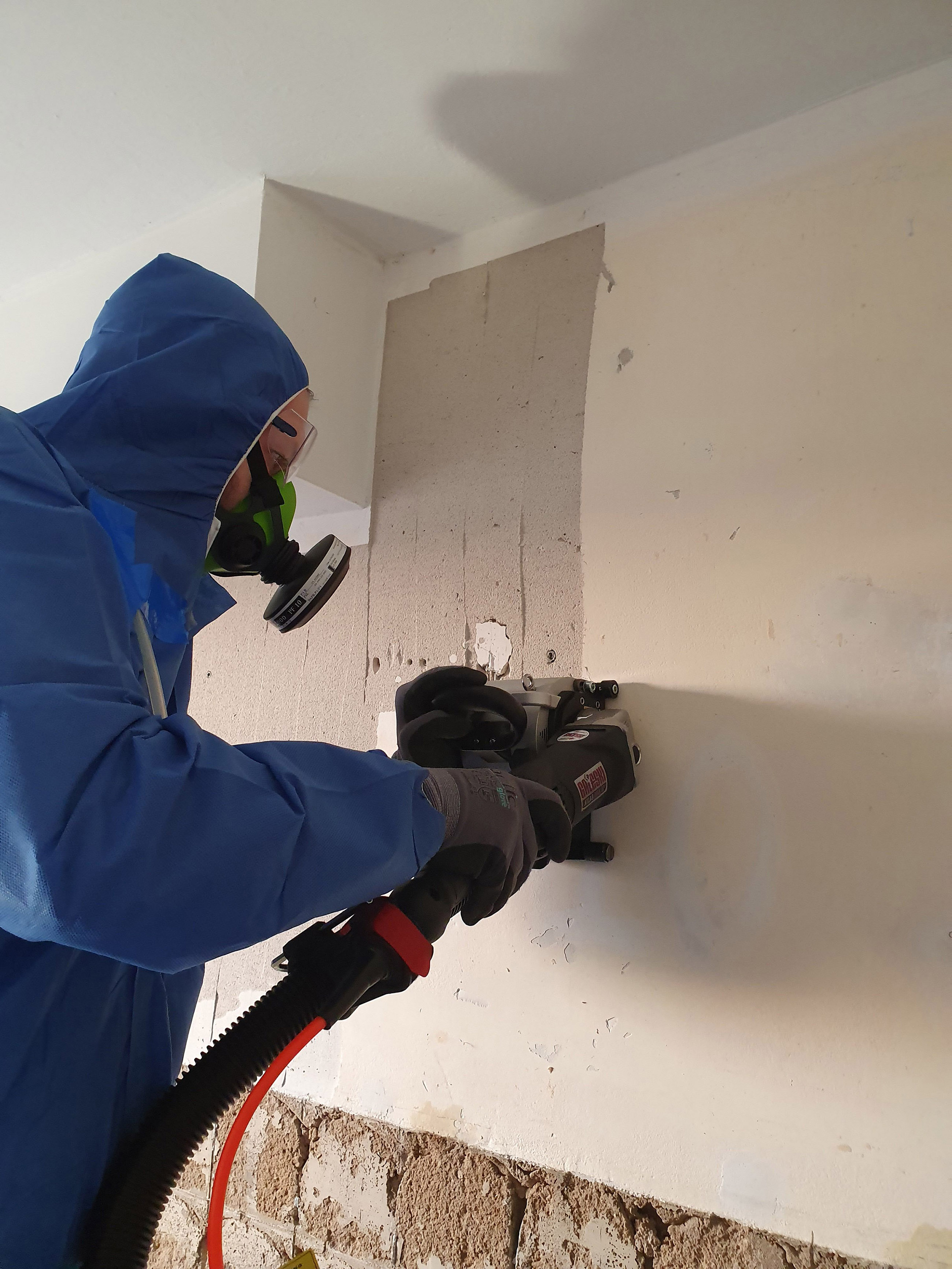 Mann in Schutzanzug bearbeitet mit einer Fräse eine Wand