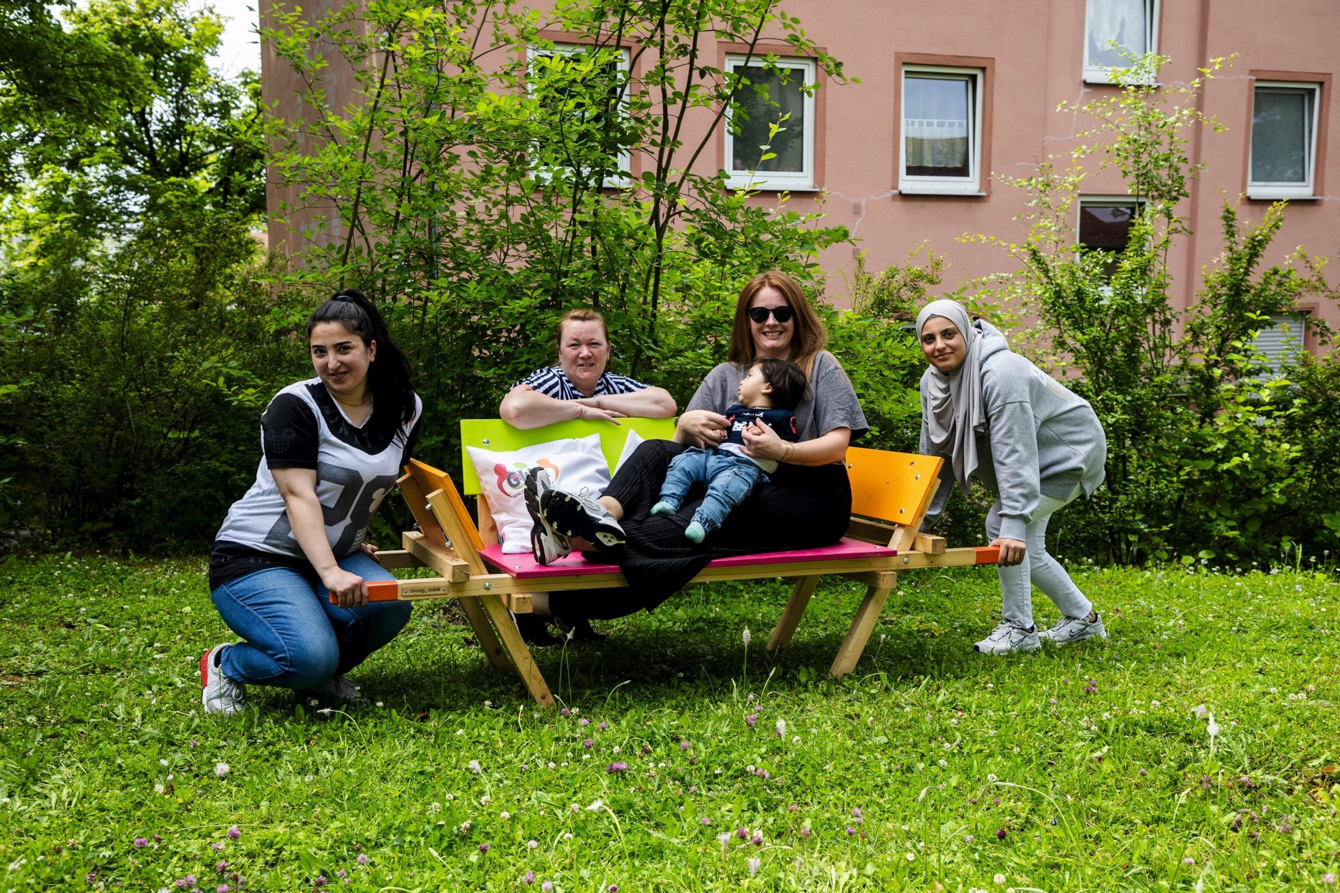 Eine Frau und ein kleines Kind sitzen auf einer bunt bemalten Bank, drei weitere Frauen hocken links, rechts und hinter der Bank