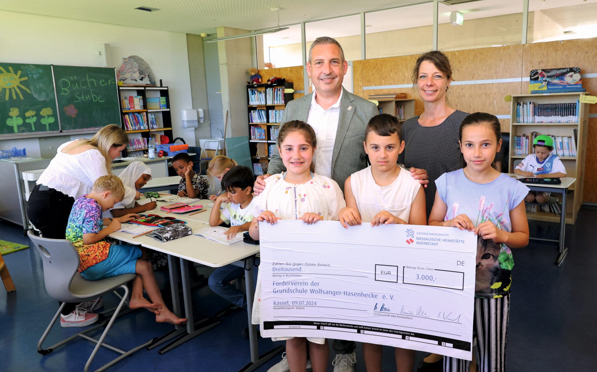 NHW-Regionalcenterleiter Sascha Holstein und Jennifer Linke von der Sozialen Quartiersentwicklung der NHW überreichen den Spendenscheck an drei Kinder.