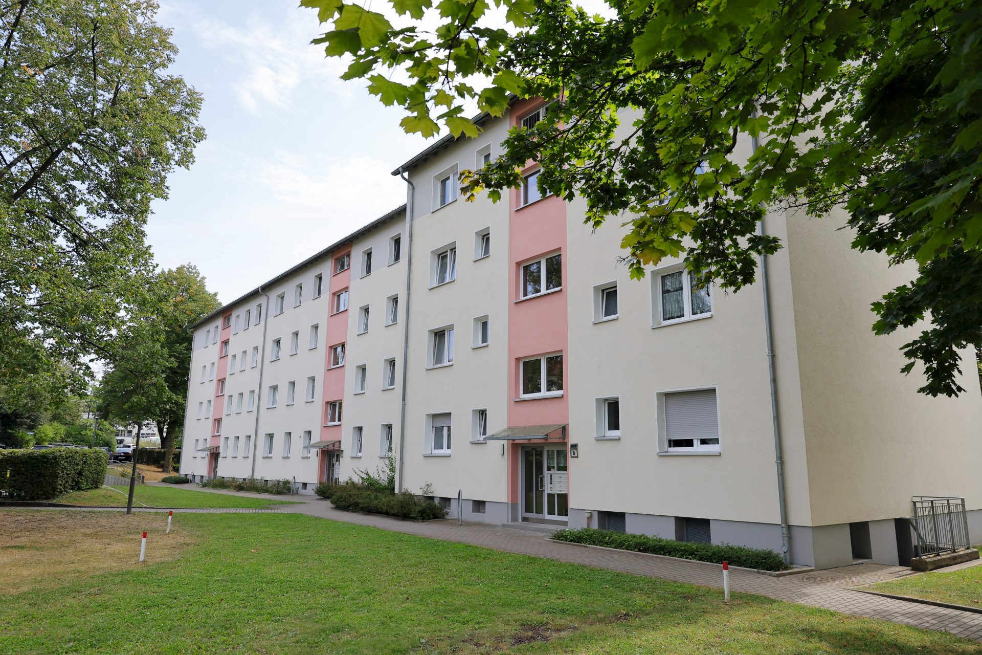 Blick auf die modernisierte Fassade eines Mehrfamilienhauses, im Vordergrund Wiese und Bäume