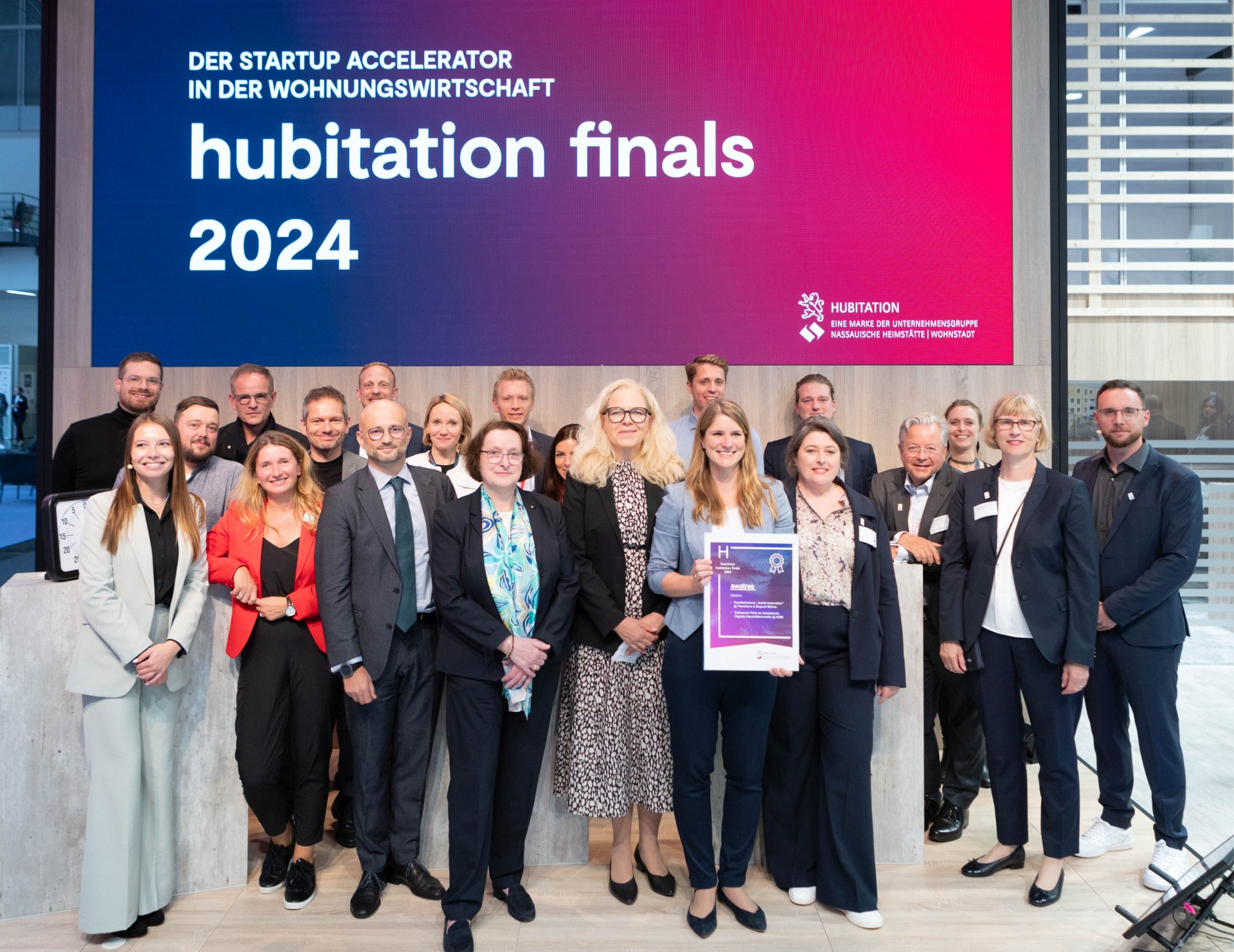 Gruppenfoto mit vielen gut gelaunten und lachenden Menschen, darüber ein Screen mit der Aufschrift "hubitation finals 2024"