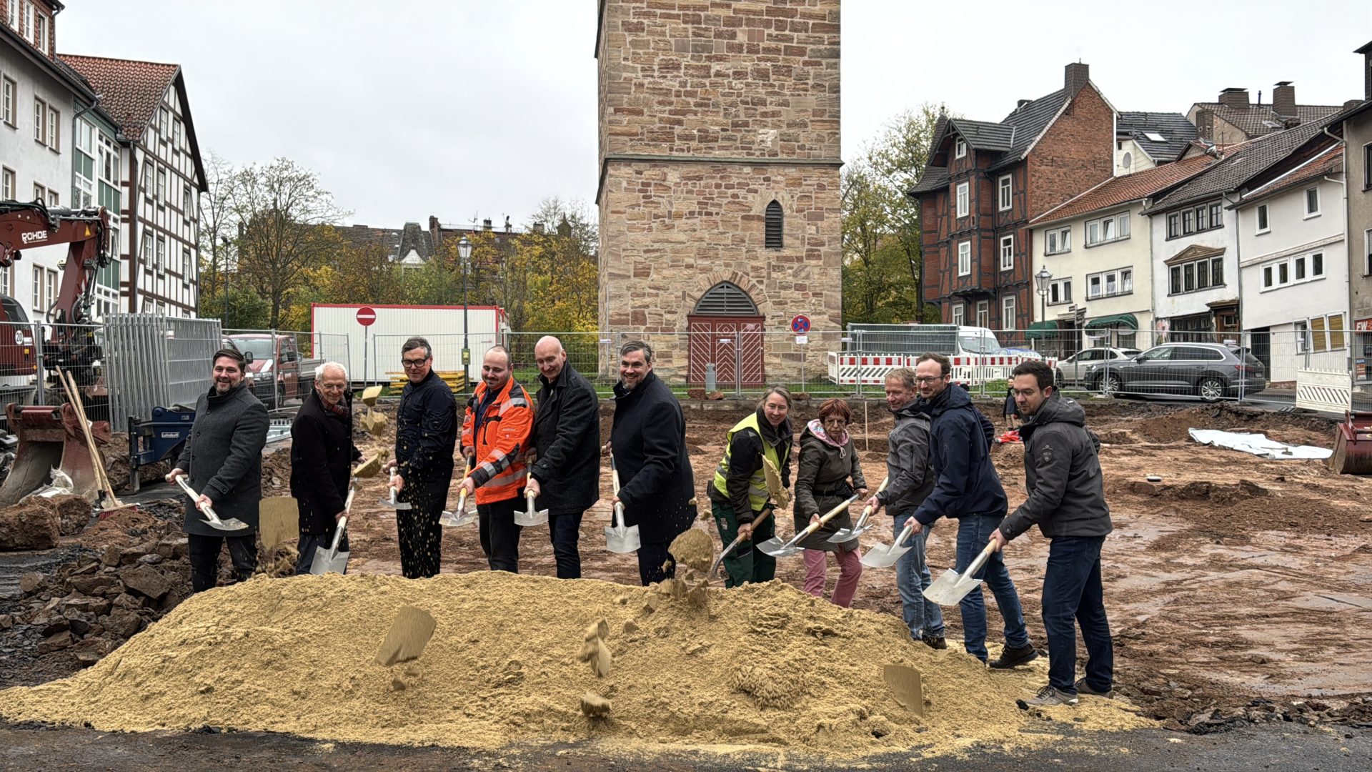 Elf Menschen mit Spaten in der Hand hinter einem Sandhaufen, hinter ihnen ein alter Turm