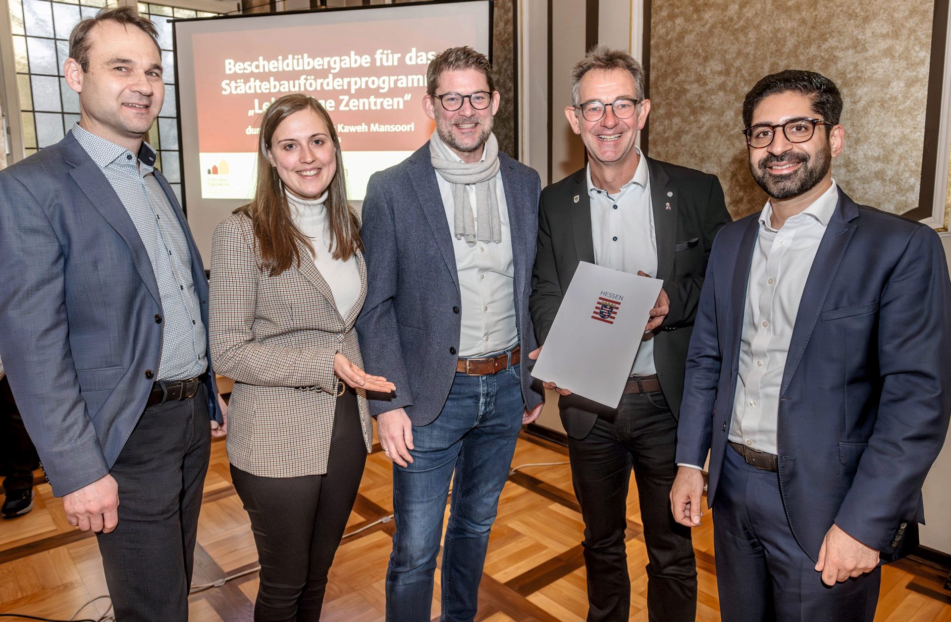 Gruppenfoto: Staatsminister Kaweh Mansoori (re.) hat einen Förderbescheid über 3,3 Millionen Euro an Bürgermeister Christian Schönung (2.v.re.) übergeben. Die ProjektStadt – (v. li.) Christian Schwarzer, Laura Pfisterer und Gregor Voss – unterstützt beim Fördermittelmanagement. 