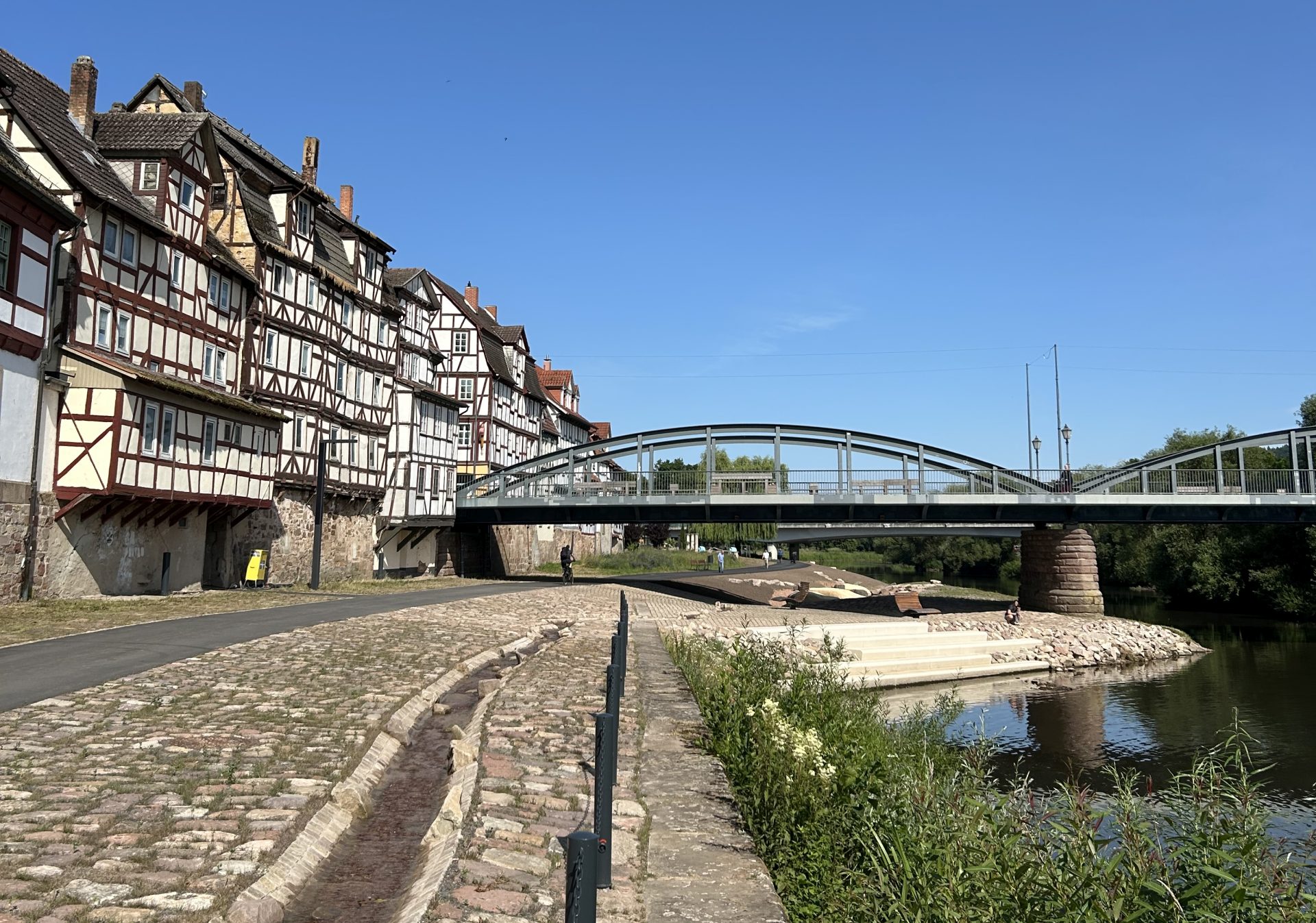 Neu gestalteter Uferbereich mit Bachlauf, rechts die Fulda, im Hintergrund Fachwerkhäuser und eine Brücke