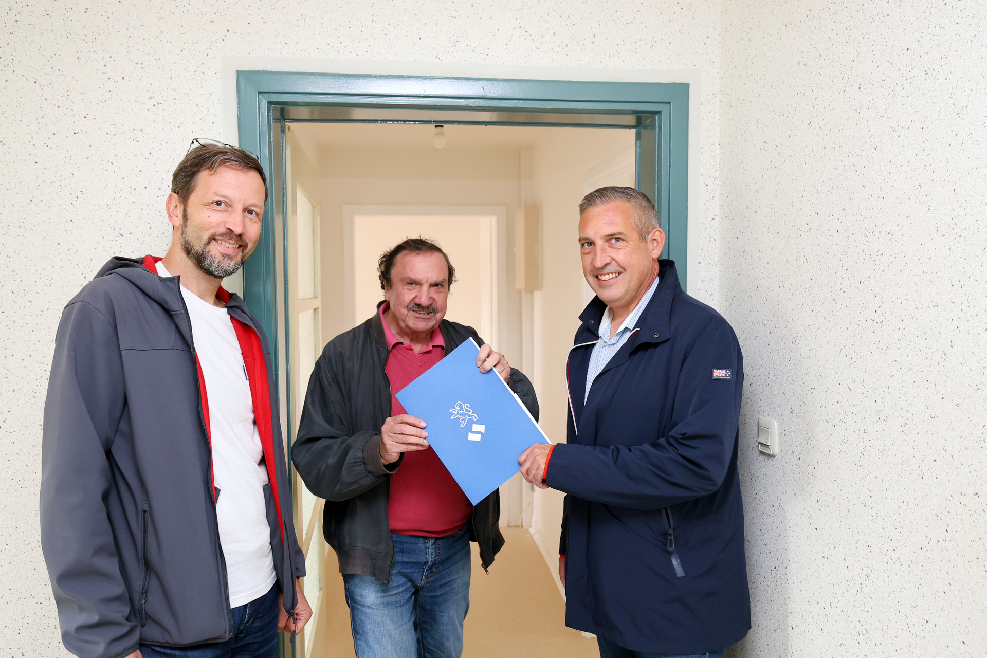 NHW-Regionalcenterleiter Sascha Holstein (re.) und Markus Beecht (li.), Geschäftsführer der Evangelischen Wohnraumhilfe, heißen Burgfried Göbel in seiner Wohnung willkommen.