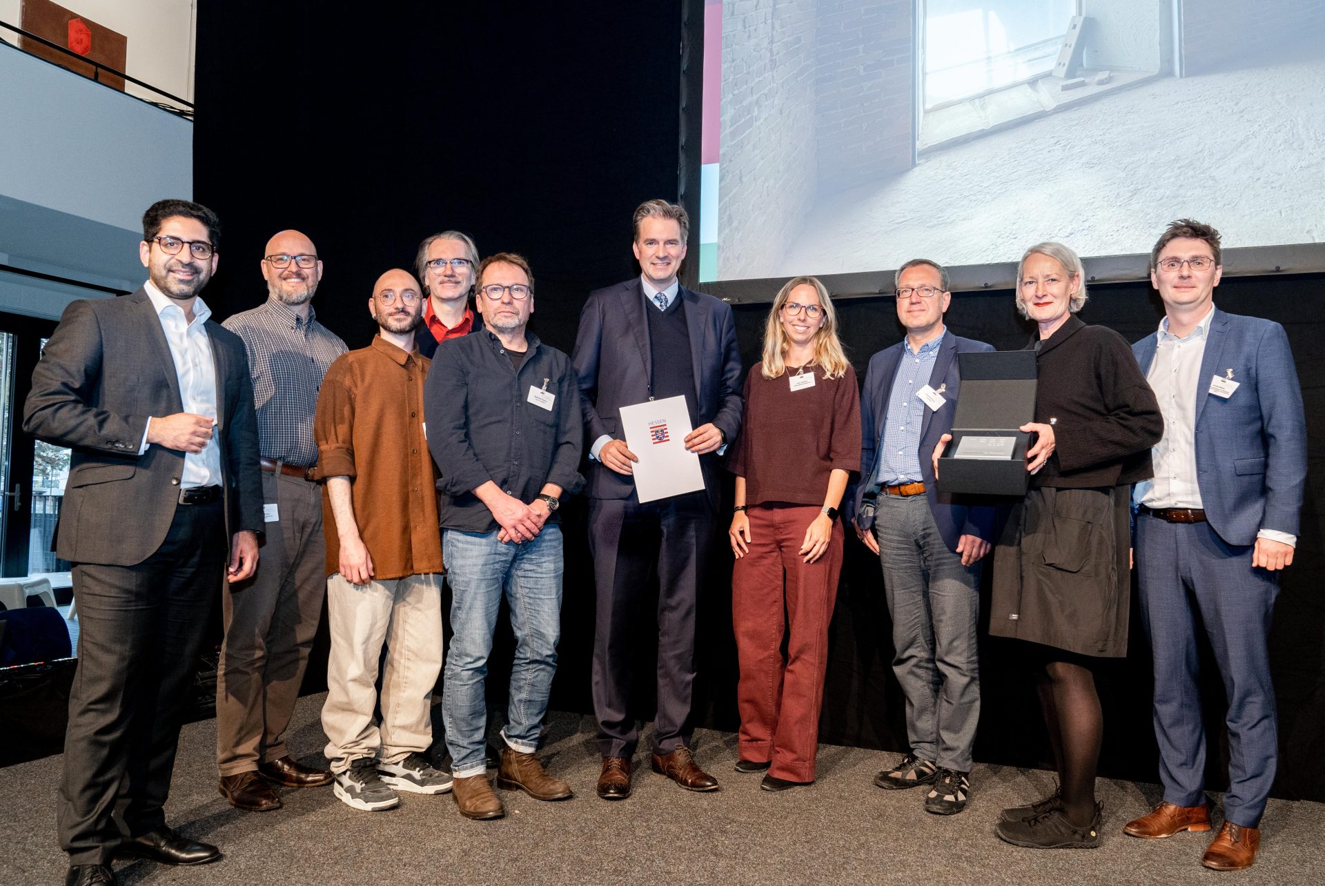 Große Bühne: Hessens Wohnungsbauminister Kaweh Mansoori (li.) übergibt den Hessischen Landespreis Baukultur 2025 für den Hochbunker Agathof im Beisein von Kassels Oberbürgermeister Sven Schoeller (Mi.) an Projektbeteiligte. 