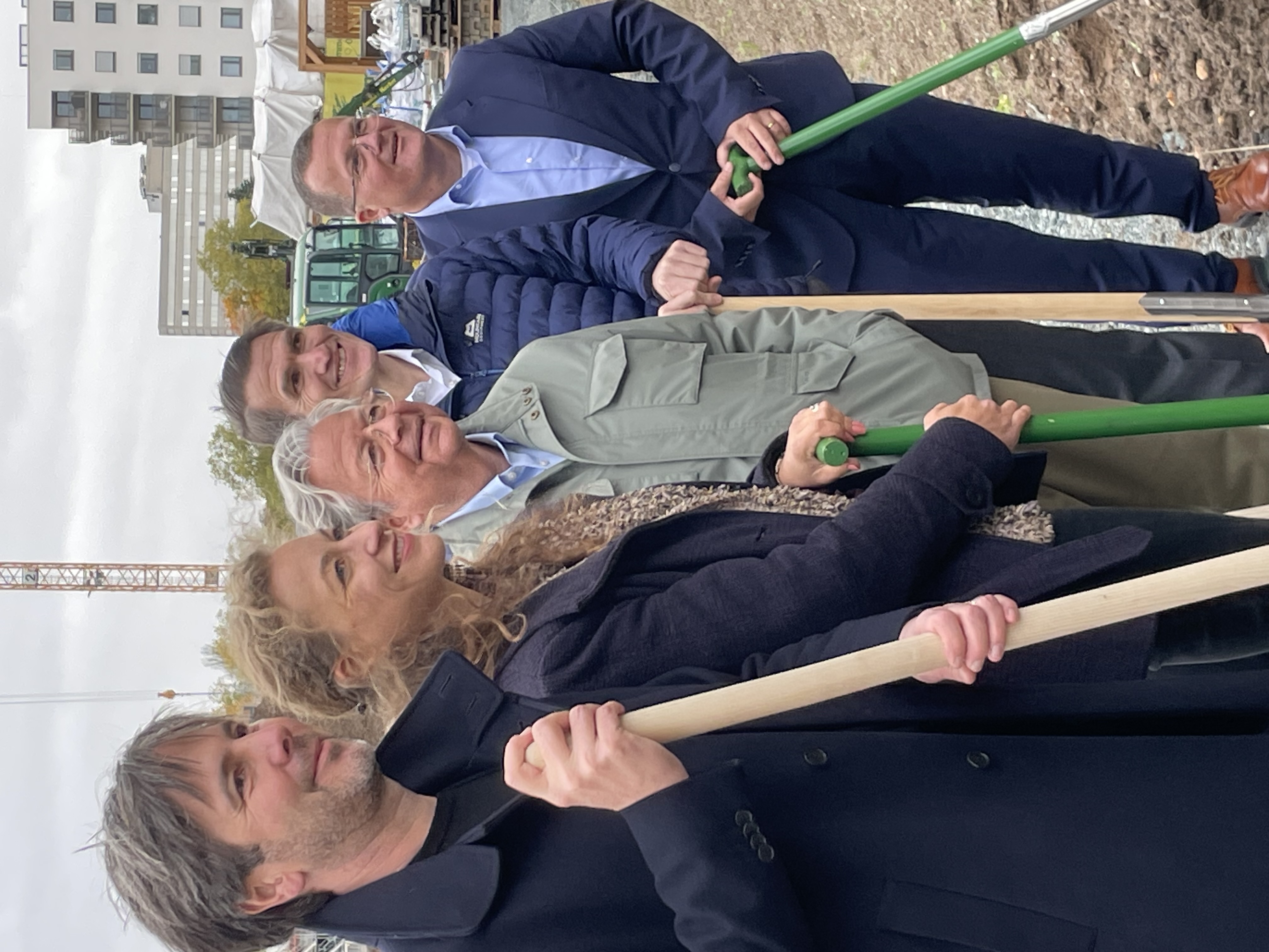 Fünf Personen mit Spaten in der Hand auf einer Baustelle im Hochformat