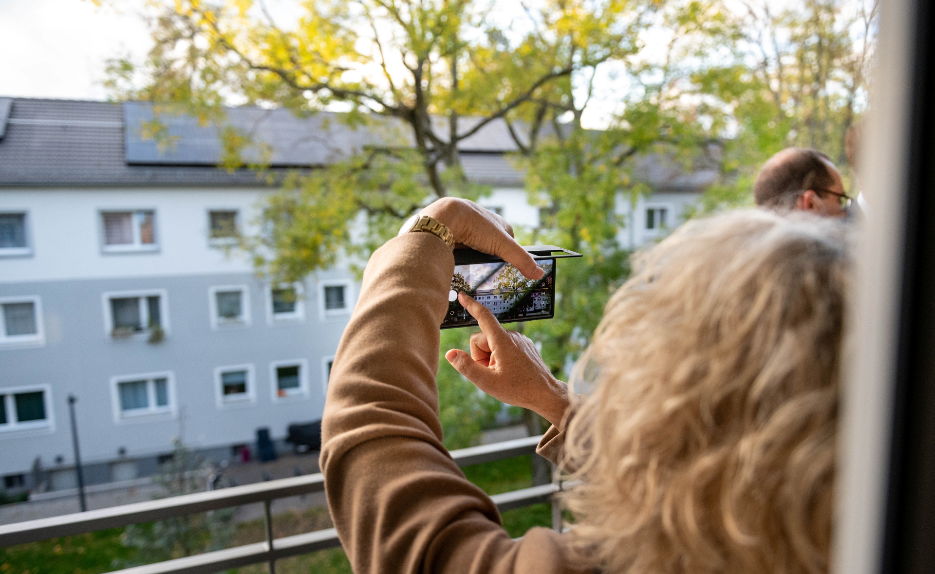 Frau macht Handyfoto von Dach mit Photovoltaik