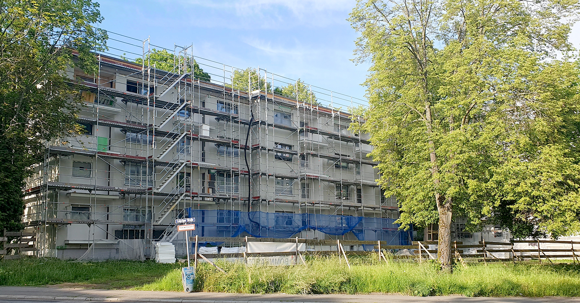 Häuserzeile in Wiesbaden-Bierstadt in der Modernisierung eingehüllt in ein Gerüst und umgeben von Bäumen.