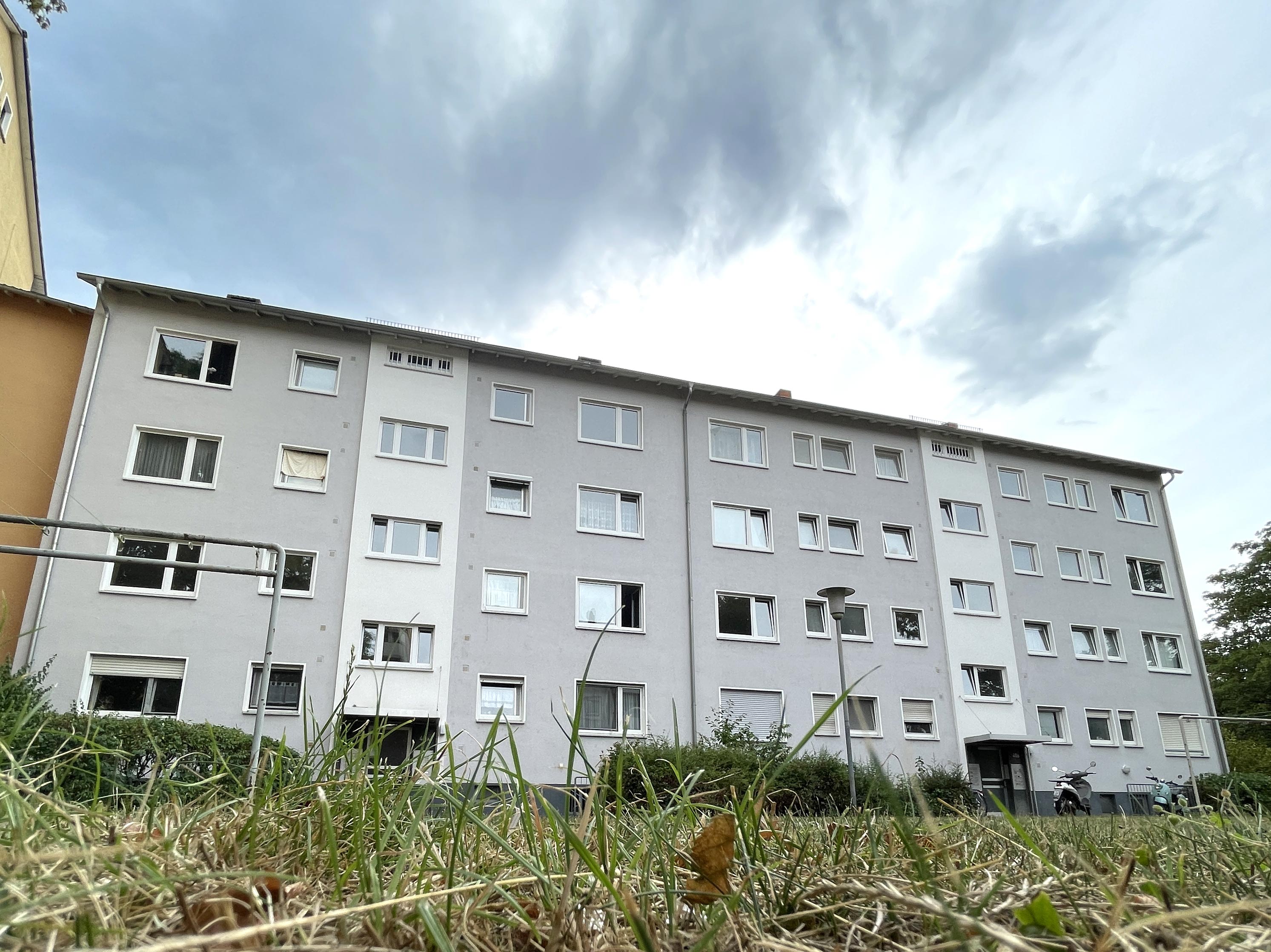 Ein Wohnhaus in verschiedenen Beigetönen vor bewölktem Himmel.