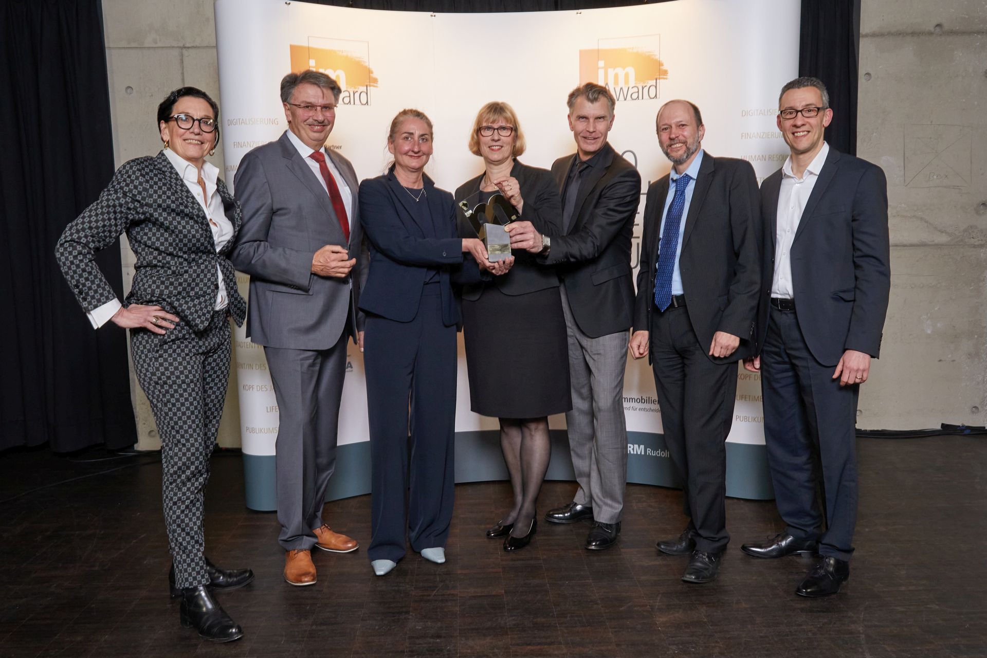 Genannte Personen, mit dem im-Award in Händen, vor einer Wand stehend.