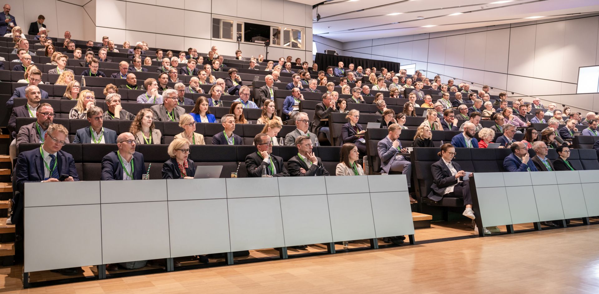 Die Ränge mit Bänken in einem hohen Raum sind voller Publikum, die gespannt zuhören.