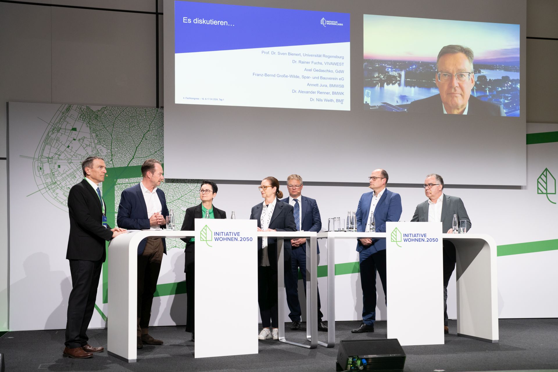 Eine Gruppe von Vertretern verschiedener Wohnungsunternehmen gehen hinter Rednerpulten in die Diskussion.