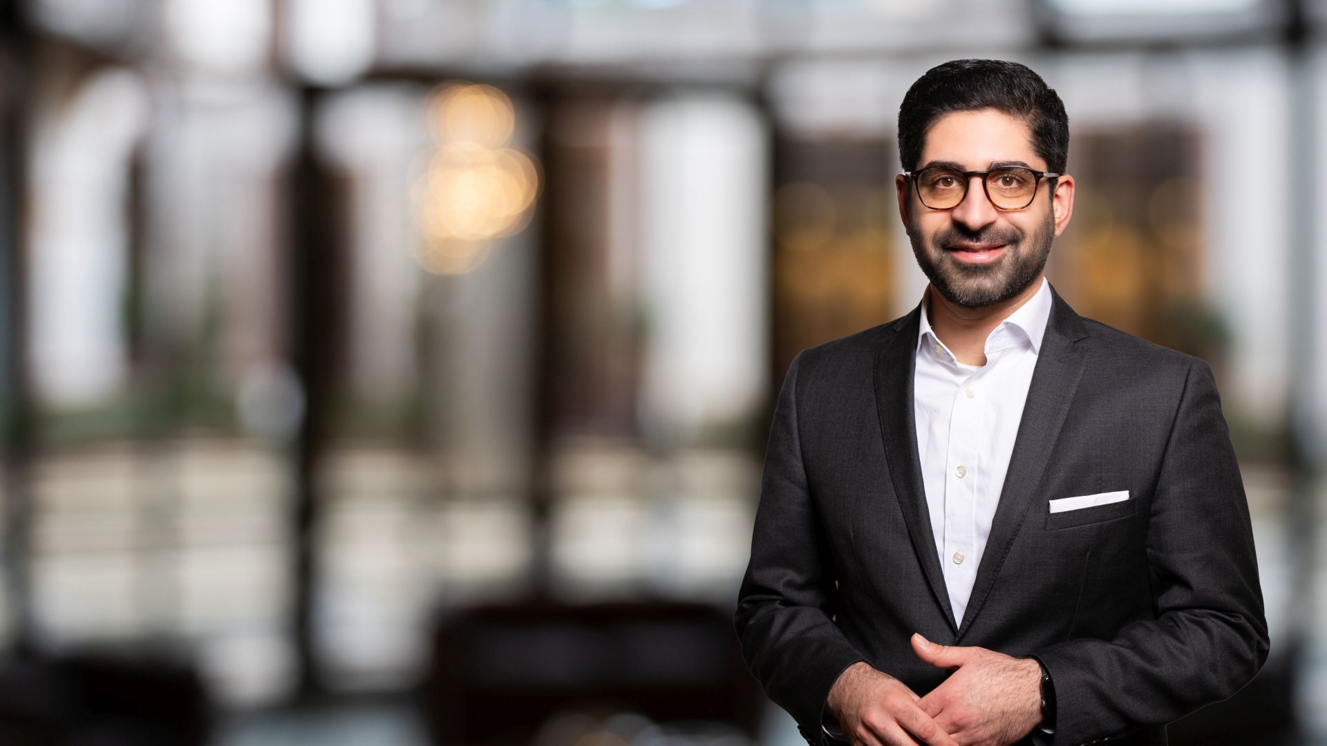 Kaweh Mansoori in einem schwarzen Anzug vor unscharfem Hintergrund.